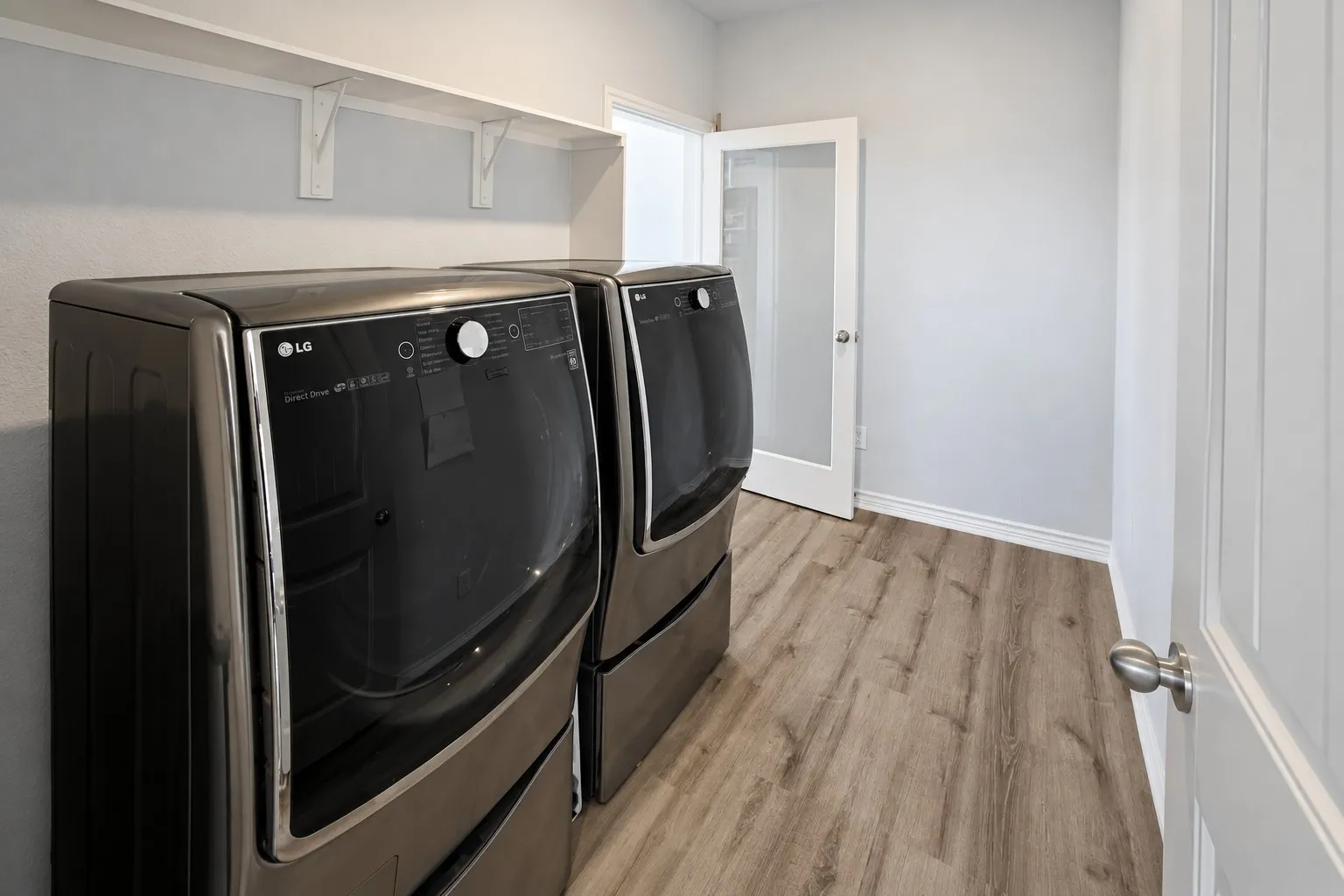 Laundry area with wood-finish flooring, overhead shelving, and a paneled interior door with a frosted glass insert