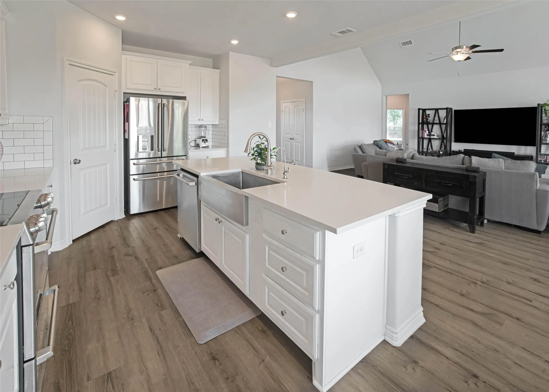 White shaker cabinetry with stainless steel appliances, a center island featuring an undermount farmhouse sink, wood-finish flooring, and recessed lighting