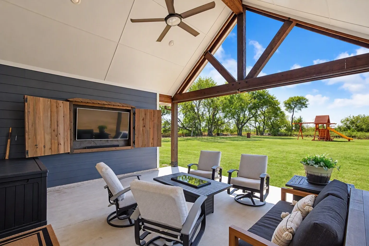 Expansive covered patio featuring a vaulted ceiling with exposed beams, ceiling fan, and built-in entertainment center with rustic wood shutters