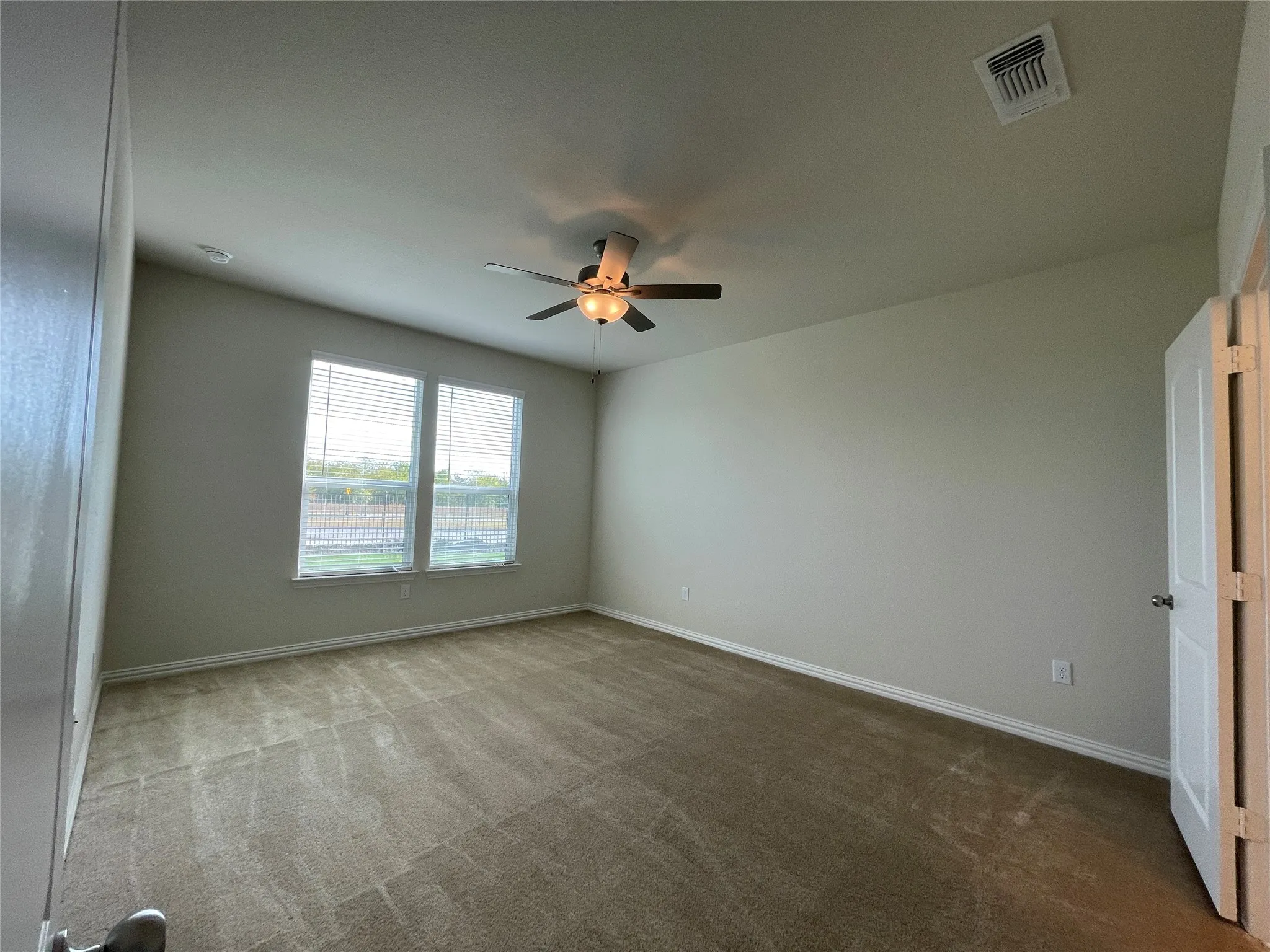 Spacious room featuring neutral carpeting, a ceiling fan with integrated lighting, and dual windows equipped with horizontal blinds