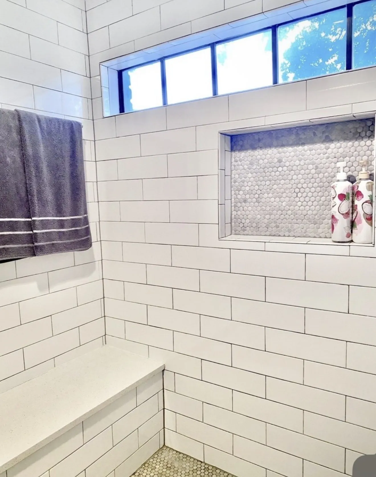 White subway tile surround, built-in bench, recessed niche with mosaic tile, transom window, and pebble-finish flooring