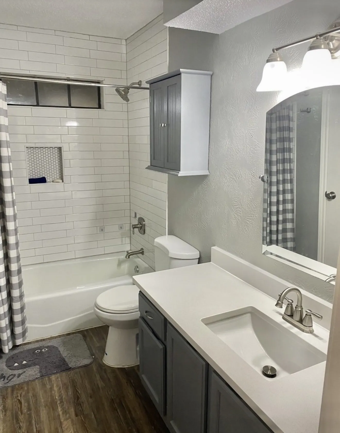 Bathroom featuring wood-finish flooring, a white subway-tiled shower surround with a recessed niche, a built-in wall cabinet, and a vanity with gray cabinetry and a white countertop