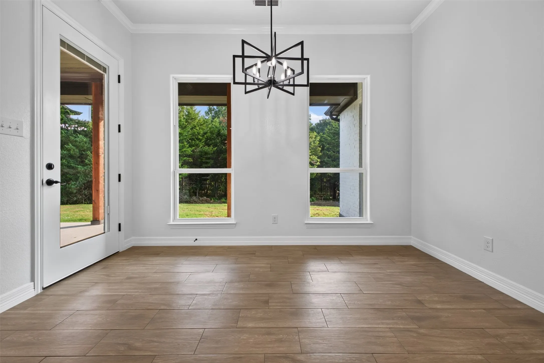 Bright dining area featuring statement lighting, large windows, and peaceful views of the backyard.