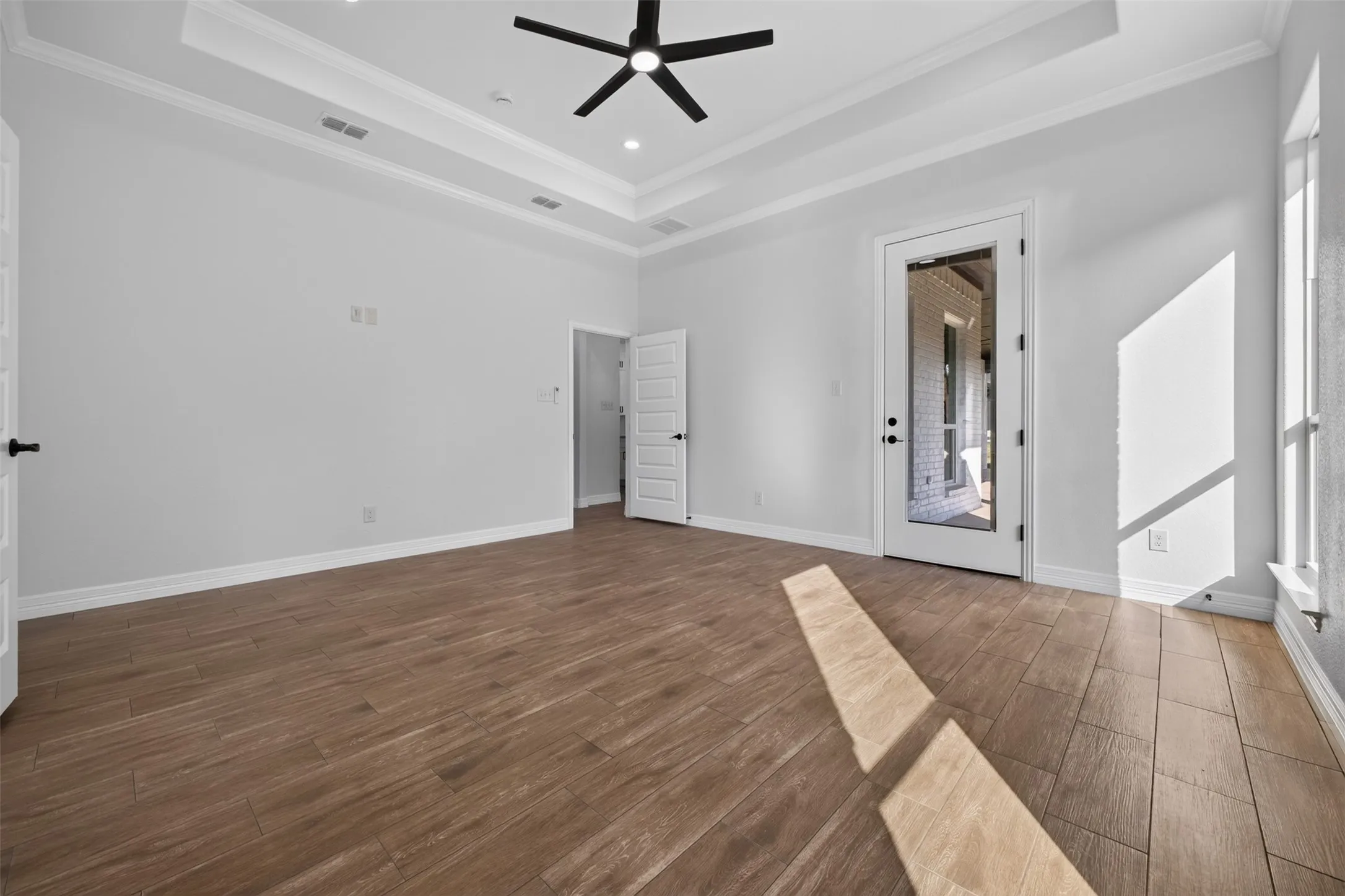 Spacious primary suite featuring dramatic tray ceiling, abundant natural light, and private access to the covered patio.