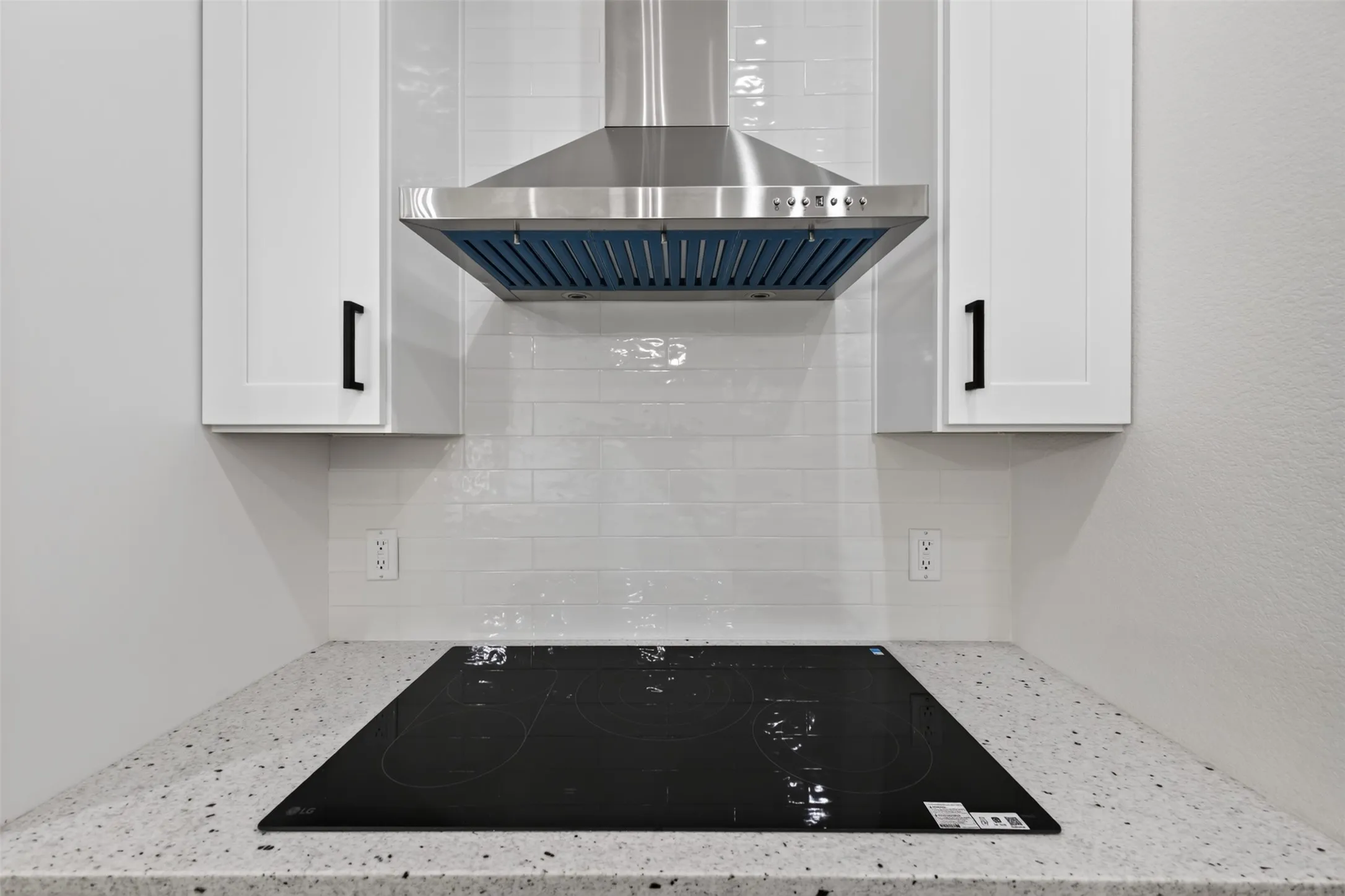 Sleek cooktop with stainless steel vent hood, tile backsplash, and quartz countertops creates a clean, modern cooking space.