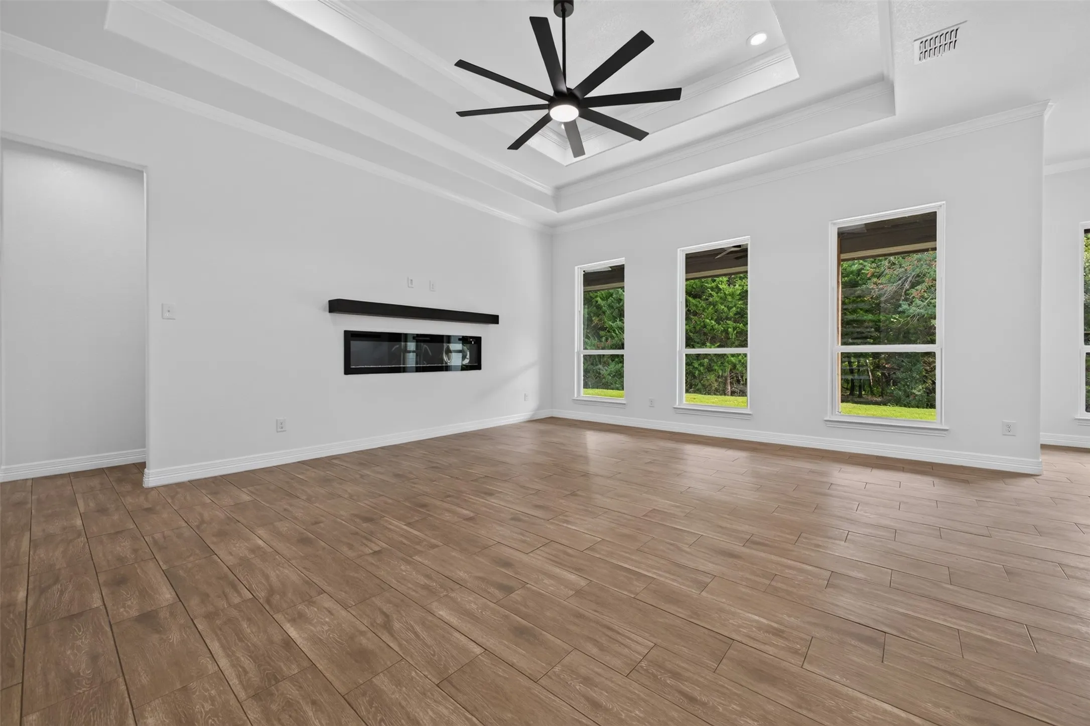 Spacious living room with soaring ceiling detail, modern fireplace, and wall of windows overlooking the tree-lined backyard.