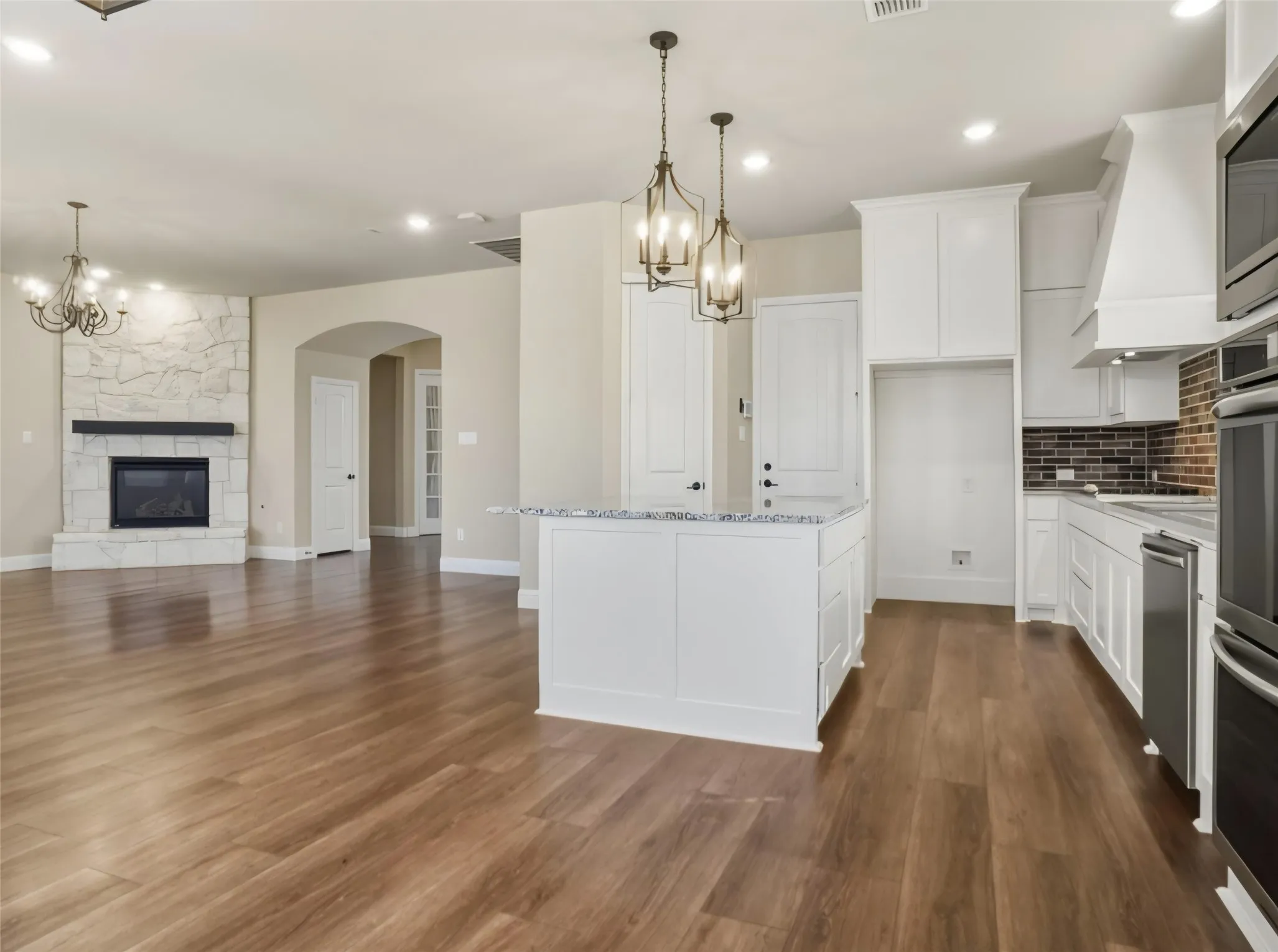 Open-concept living space with wood-finish flooring, a stone-surround fireplace with a black mantel, and an arched entryway