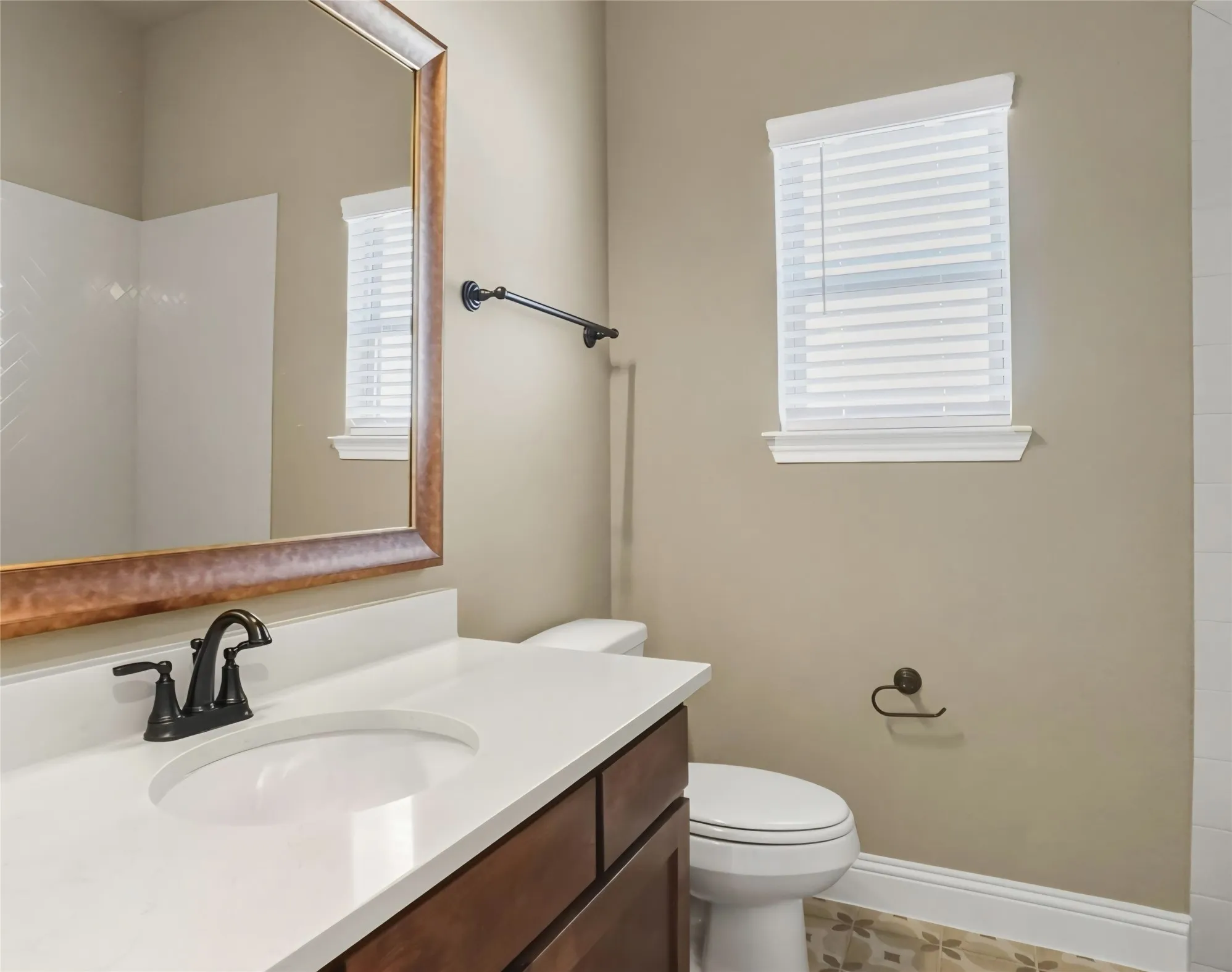 Bathroom featuring a white integrated sink, dark wood-finish cabinetry, a bronze-framed mirror, and a window with blinds