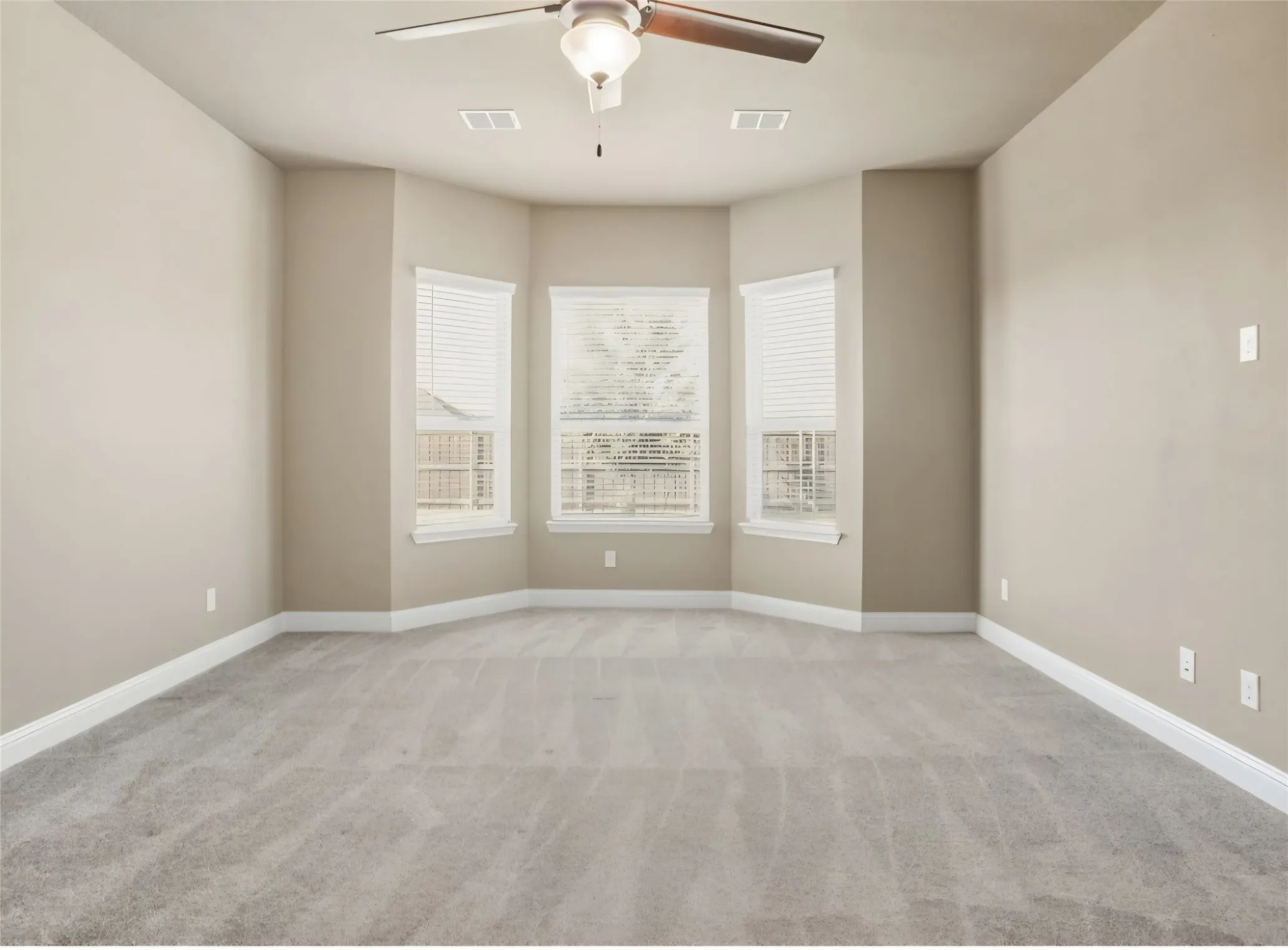 Expansive room featuring carpet flooring, bay windows with blinds, a ceiling fan, and neutral wall tones