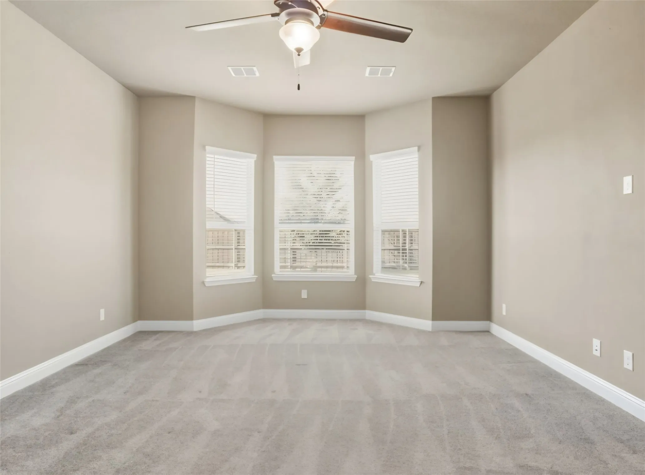 Bay window with three windows, neutral wall paint, ceiling fan with integrated lighting, and light-toned carpet flooring