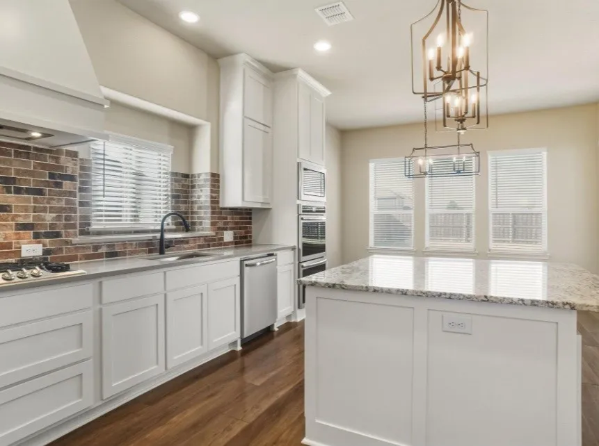 White shaker-style cabinetry, a brick-finish backsplash, and stainless steel appliances define this kitchen