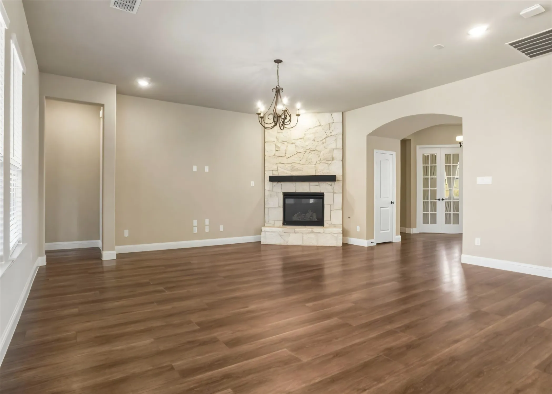 Spacious living area featuring wood-finish flooring, a stone-clad fireplace with a dark mantel, and recessed lighting