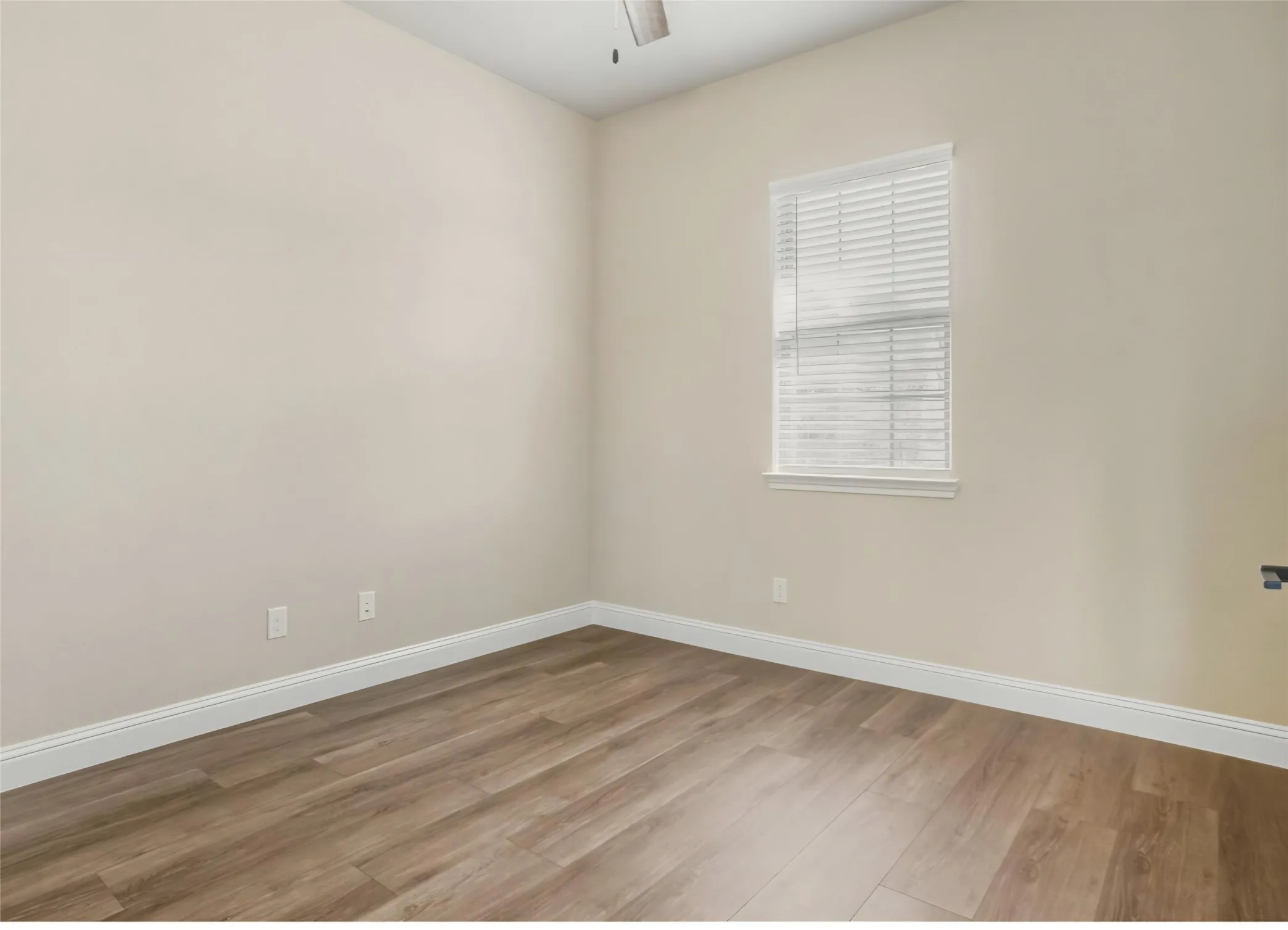 Wood-finish flooring with white baseboards, a window with blinds, and light-colored walls