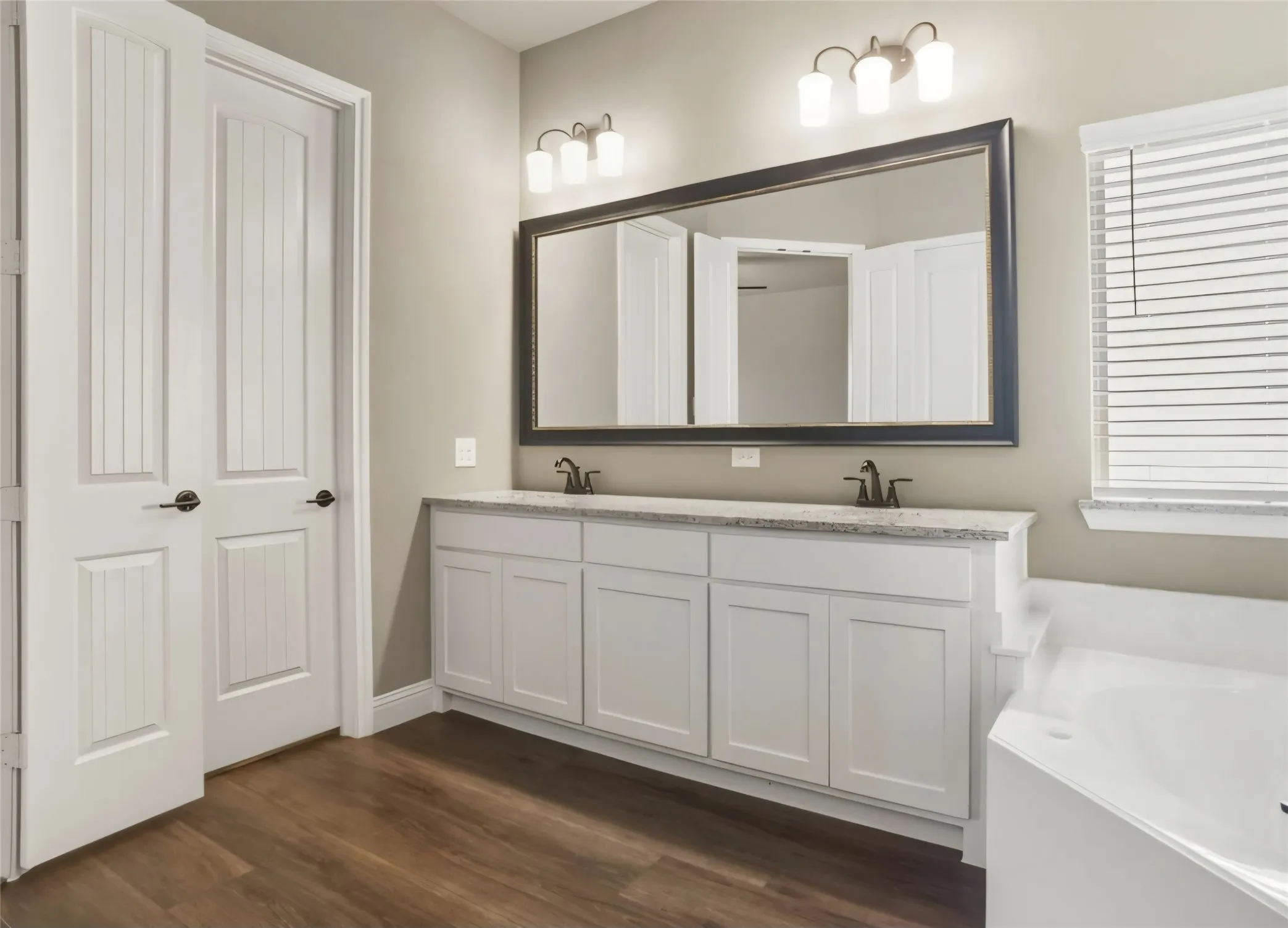 Wood-finish flooring, dual white vanities with light-toned countertops, and an integrated corner soaking tub