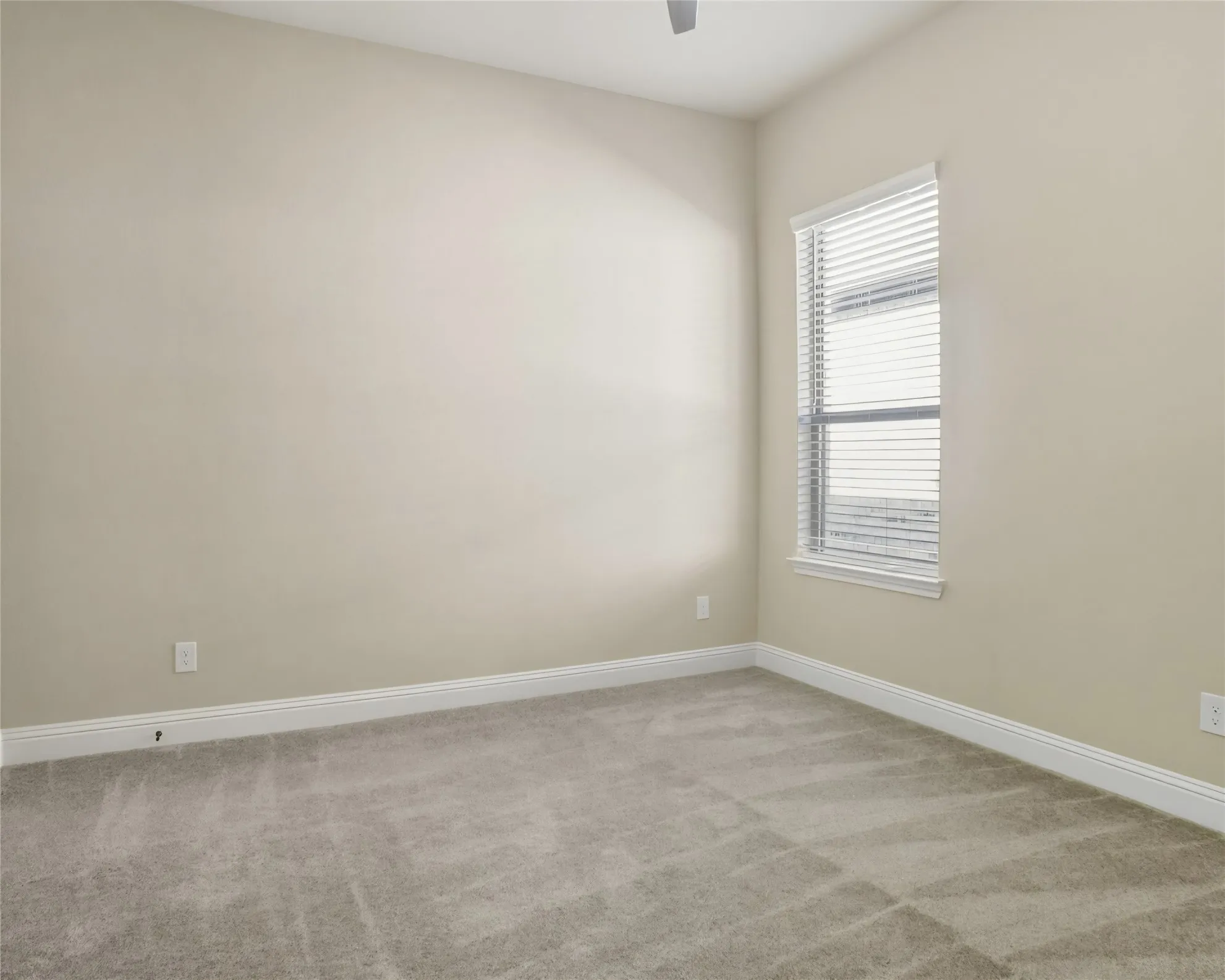 Neutral tone wall paint, light gray carpeting, white window blinds, and a ceiling fan