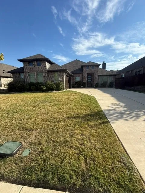Brick veneer exterior with dark shingle roofing, integrated garage, concrete driveway, and front landscaping