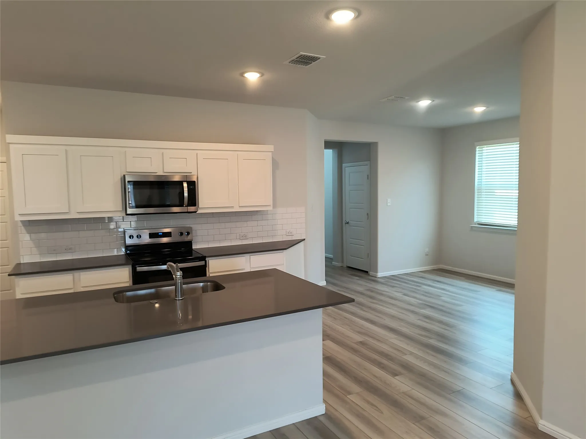 Modern kitchen featuring white shaker cabinetry, stainless steel appliances, subway tile backsplash, and a large island with an undermount sink