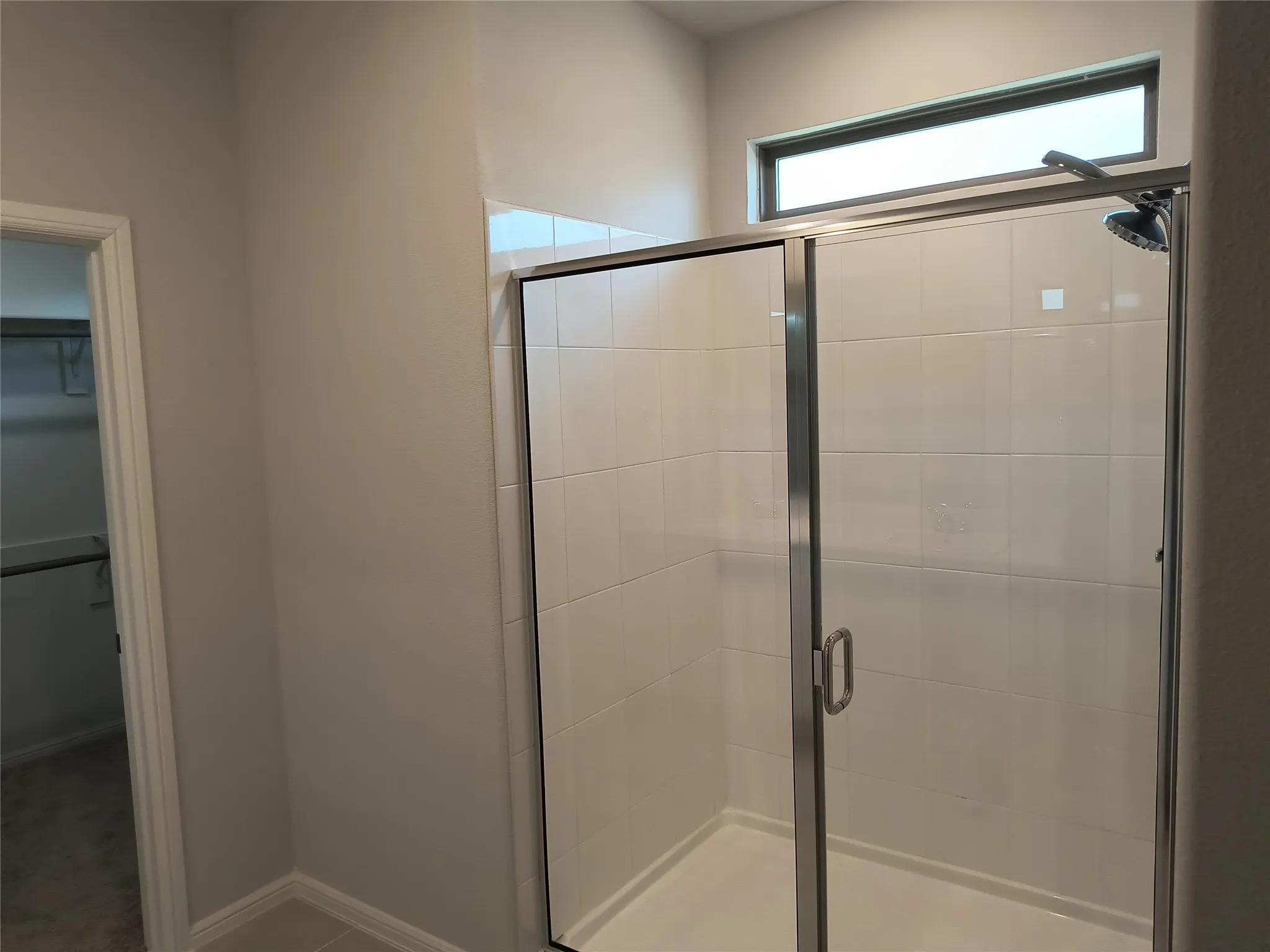 Tiled shower with a sliding glass door enclosure and a high transom window
