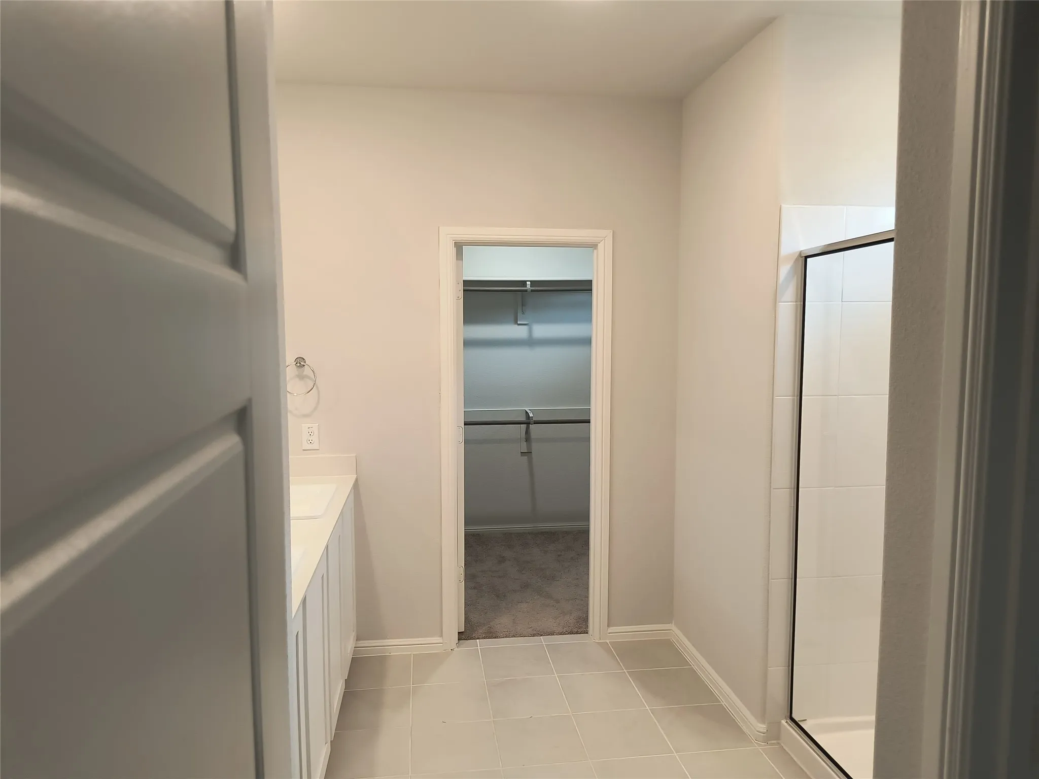 White vanity with integrated sink, tile flooring, and a walk-in shower with glass enclosure