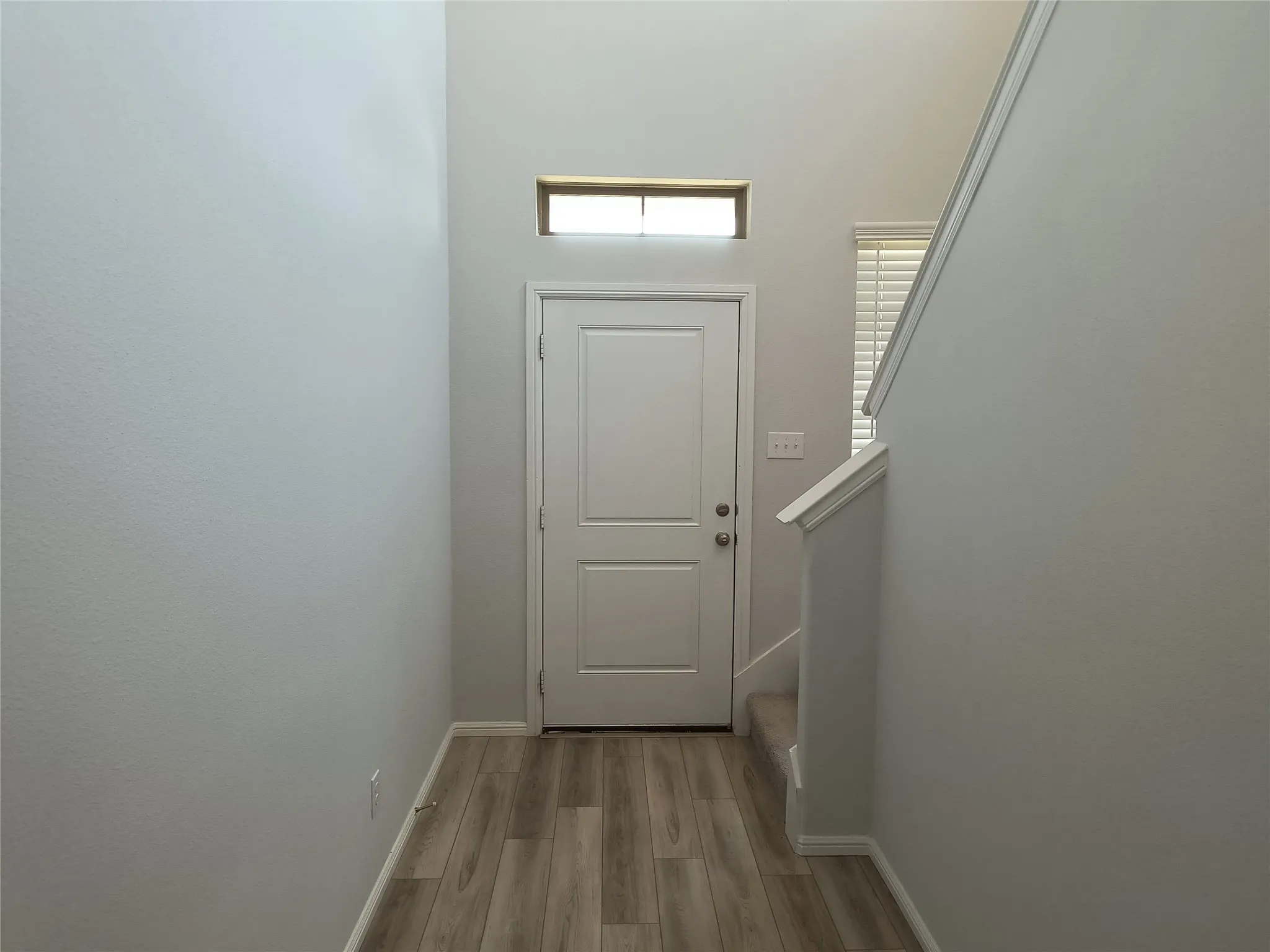 Entryway with wood-finish flooring, white paneled door, transom window, and a carpeted staircase