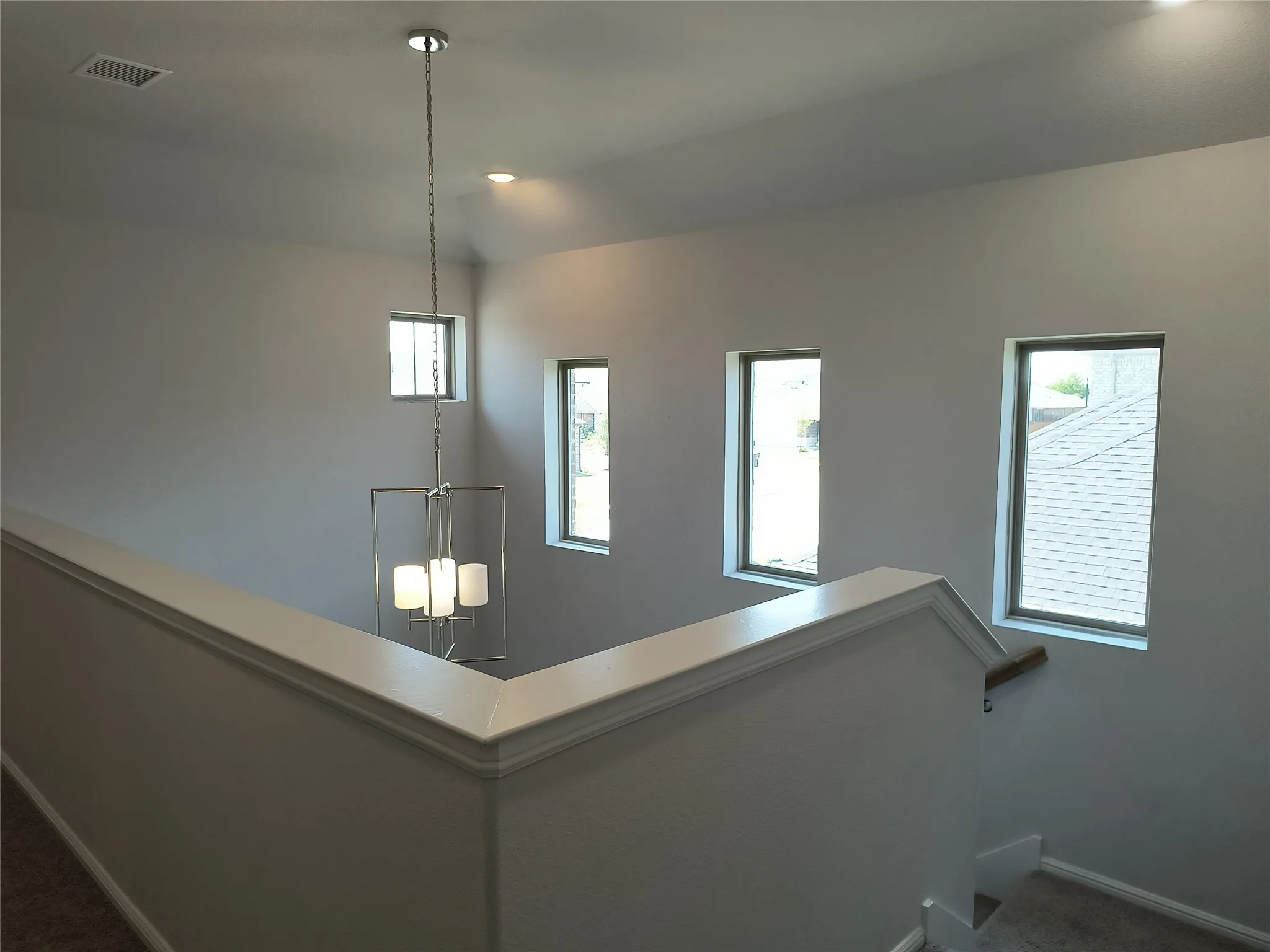 Open-concept staircase with a white railing, contemporary chandelier, recessed lighting, and multiple windows