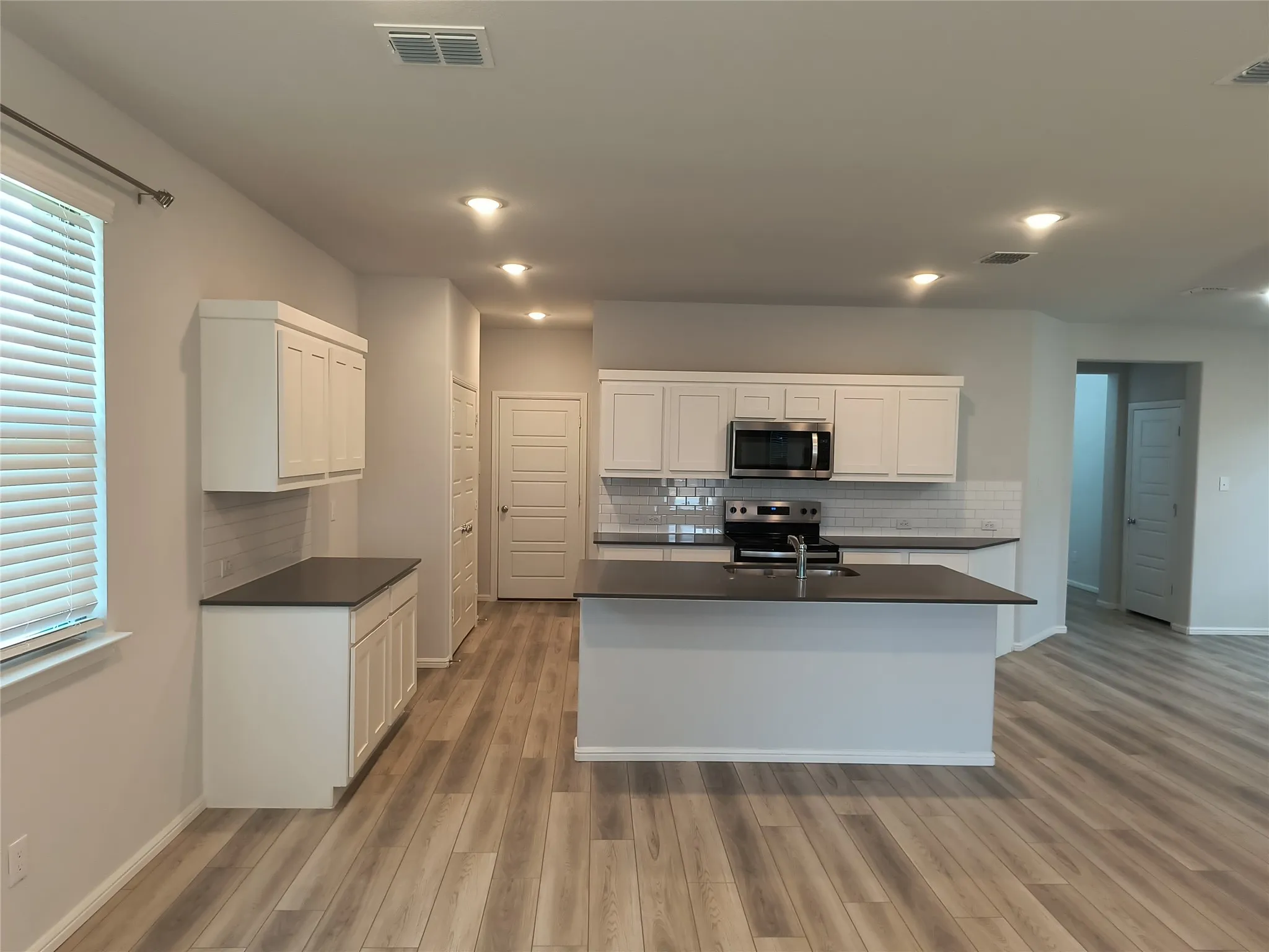 Open-concept kitchen with wood-finish flooring, white cabinetry, dark countertops, and stainless steel appliances