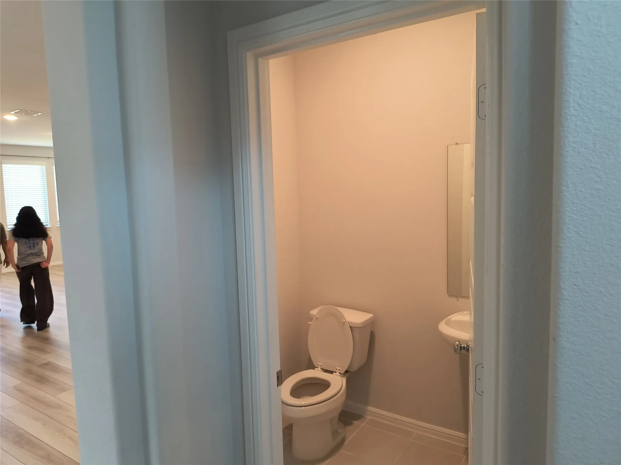 Pedestal sink with mirror, tile flooring, and a white toilet