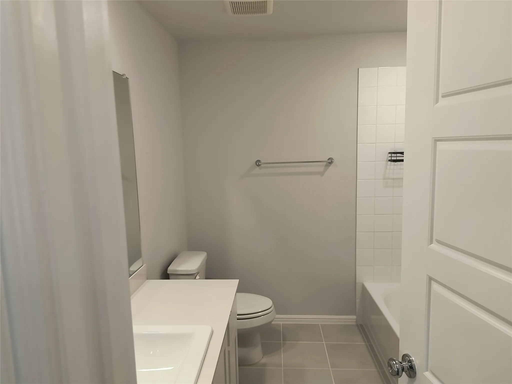 Bathroom featuring a white vanity with an integrated sink, polished chrome fixtures, a toilet, a bathtub with white subway tile surround, and neutral floor tiling