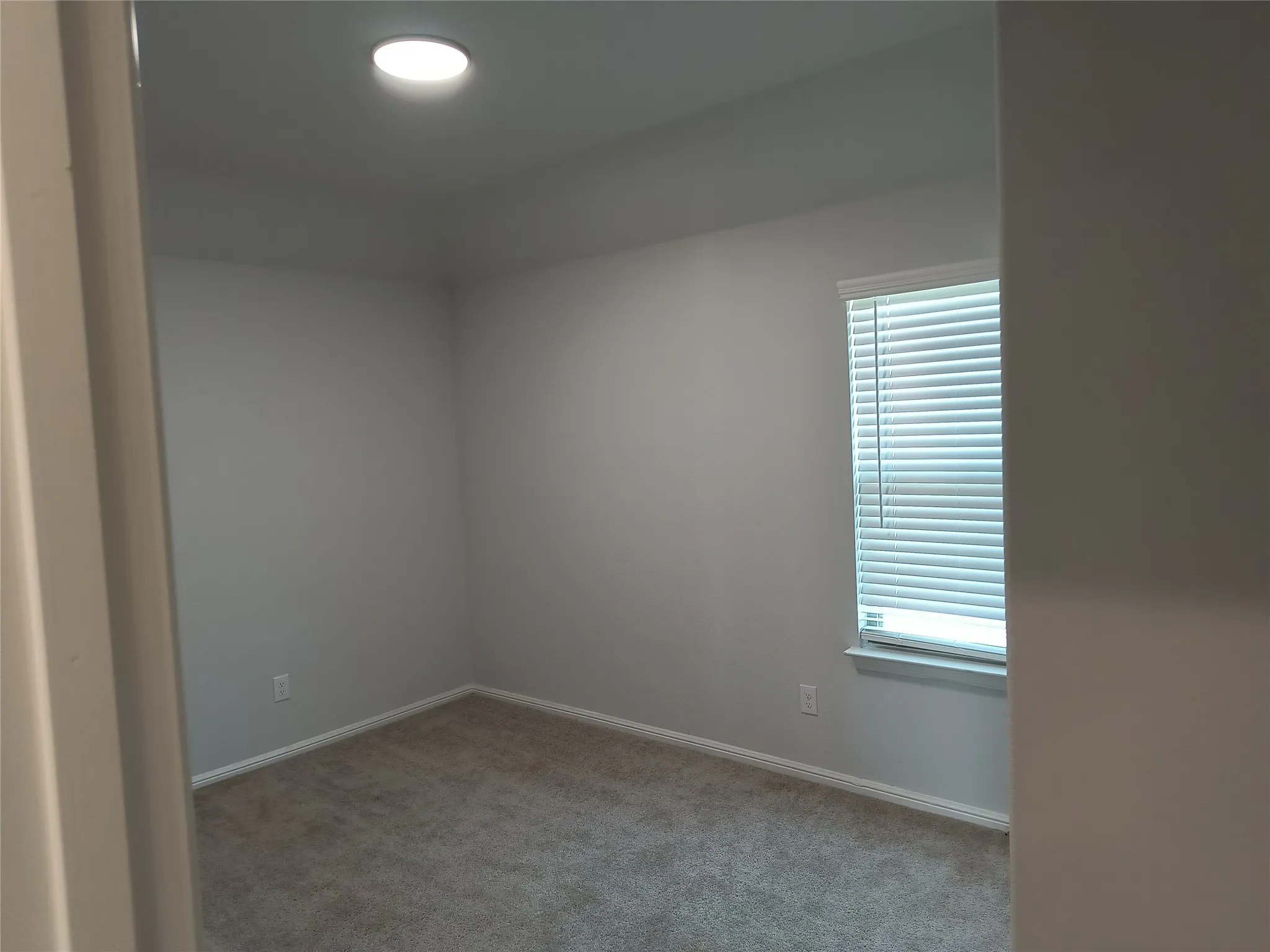 Recessed ceiling lighting, a window with horizontal blinds, and neutral-toned wall-to-wall carpeting