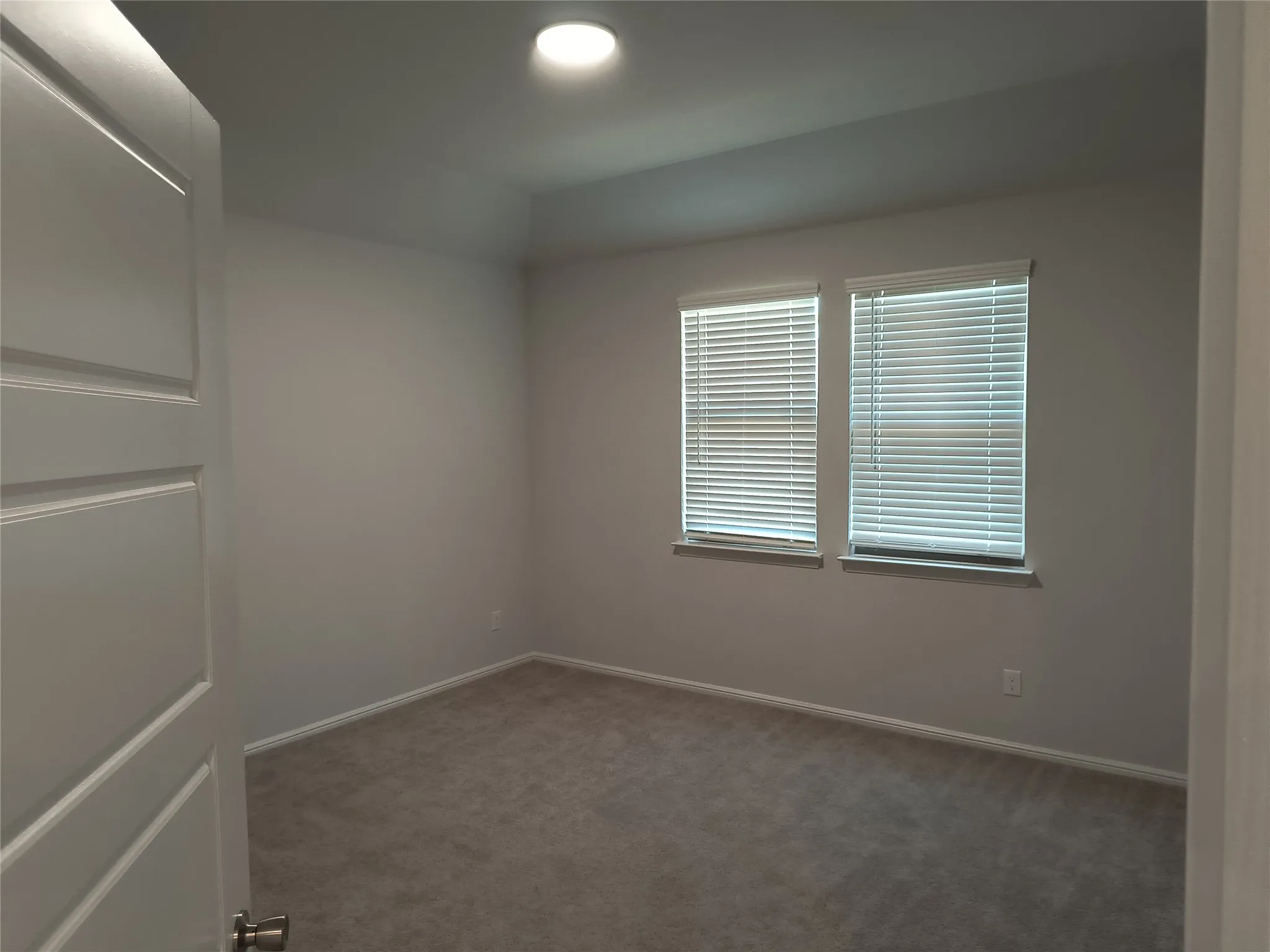 Recessed lighting, two windows with blinds, light gray wall color, and gray carpet flooring