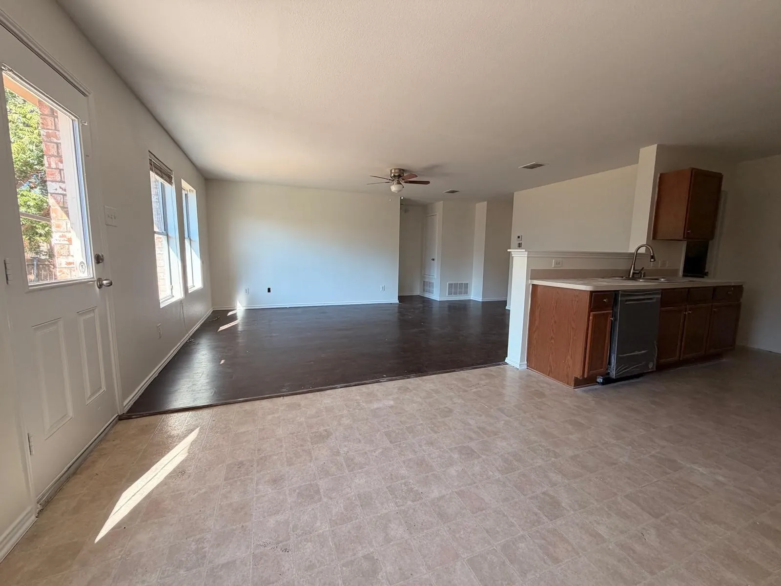 Open concept living area with diverse flooring, a ceiling fan, and multiple windows