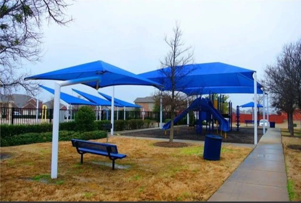 Outdoor recreation area featuring multiple shade structures, playground equipment, and a paved pathway