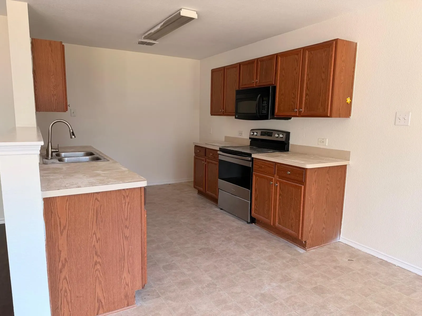 Kitchen featuring wood-finish cabinetry, stainless steel appliances, laminate countertops, a double basin sink with a gooseneck faucet, and vinyl flooring