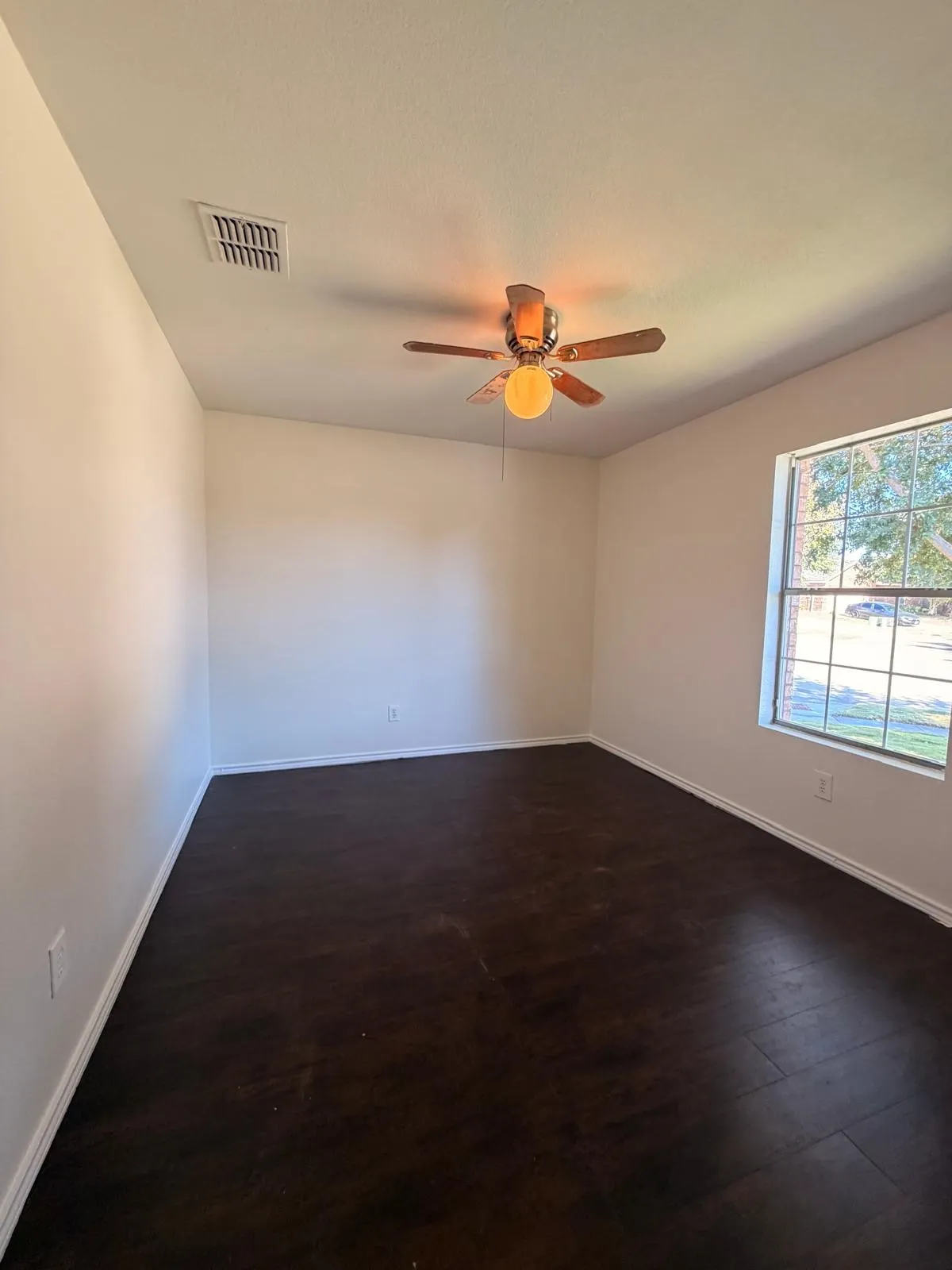 Dark wood-finish flooring, a ceiling fan with integrated lighting, and a single window with grilles