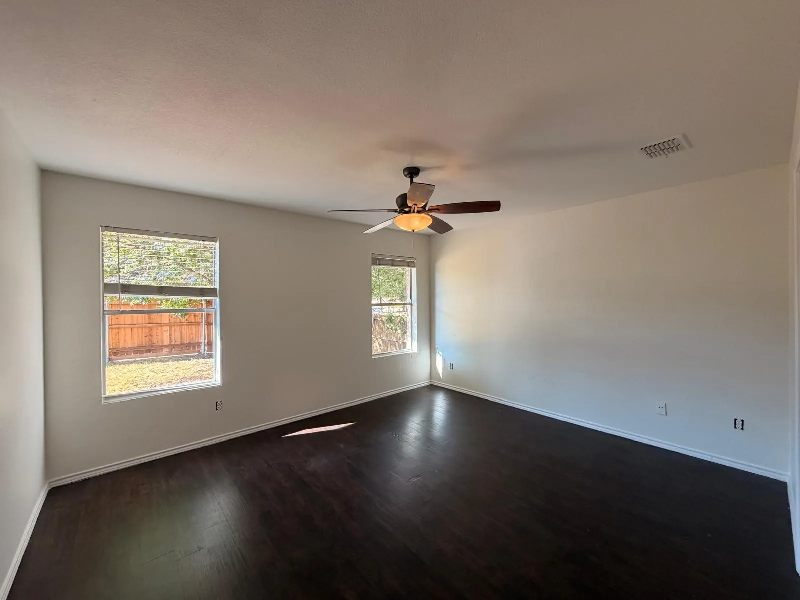 Room featuring dark wood-finish flooring, two windows, a ceiling fan with integrated lighting, and light-colored walls