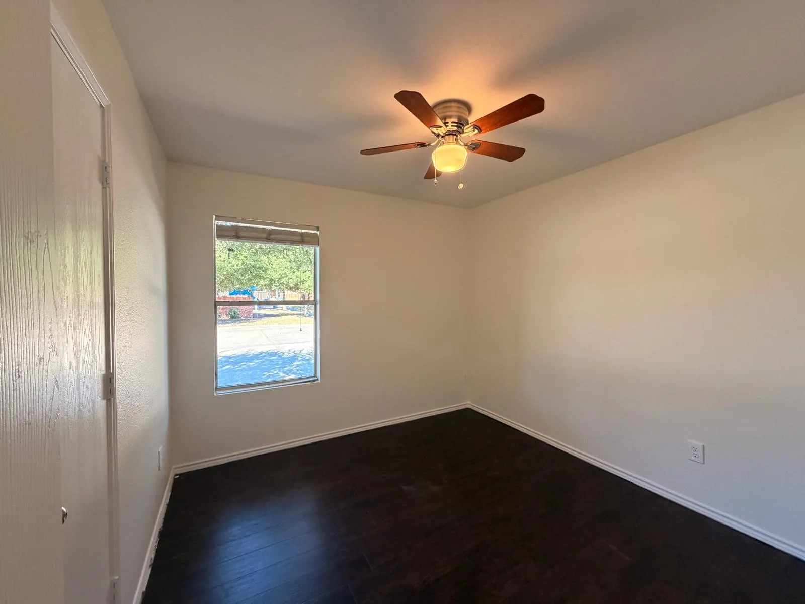 Wood-finish flooring with light-toned walls, a single window, and a ceiling fan with integrated lighting