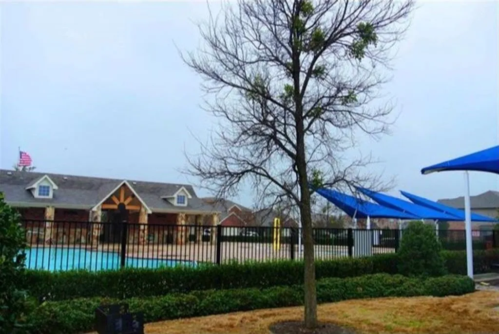 Community clubhouse featuring a stone facade and dormer windows, alongside a fenced swimming pool with blue shade structures
