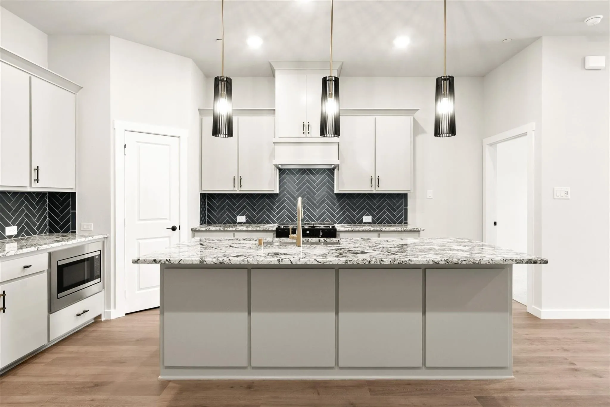 Kitchen with backsplash, light wood-style floors, an island with sink, hanging light fixtures, and stainless steel microwave