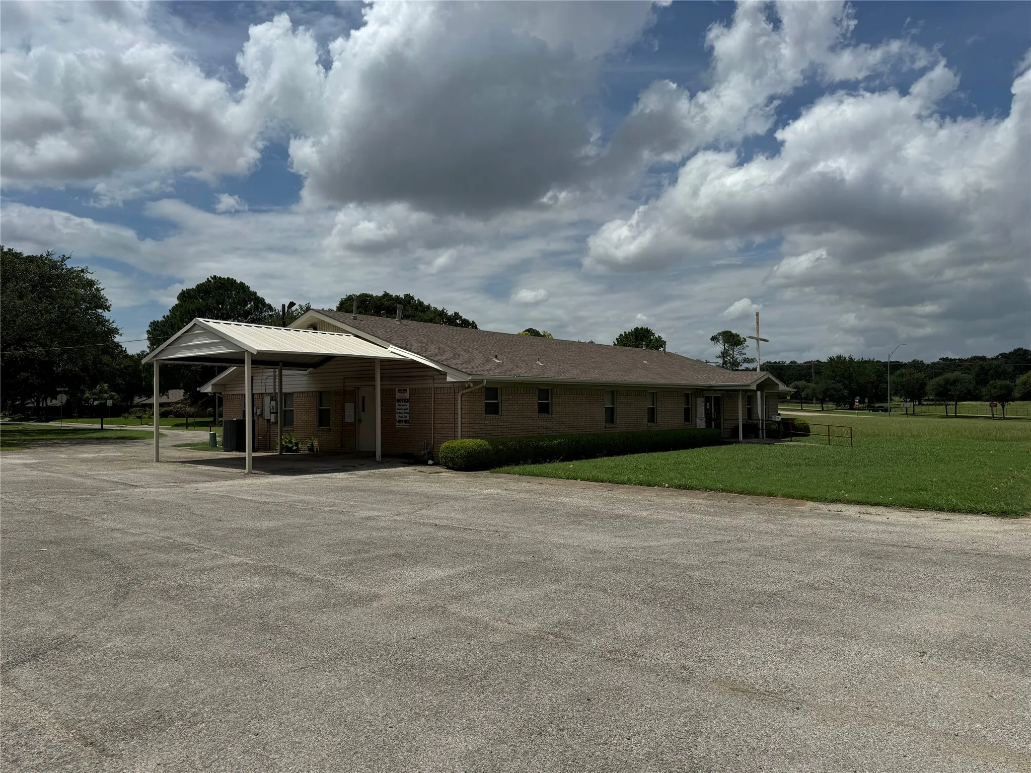 Brick exterior with a peaked roof, covered entryway, and an expansive paved parking area