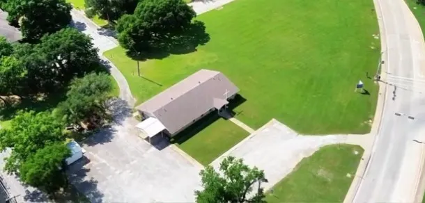 Building with a pitched roof, adjacent paved parking areas, and surrounding green spaces