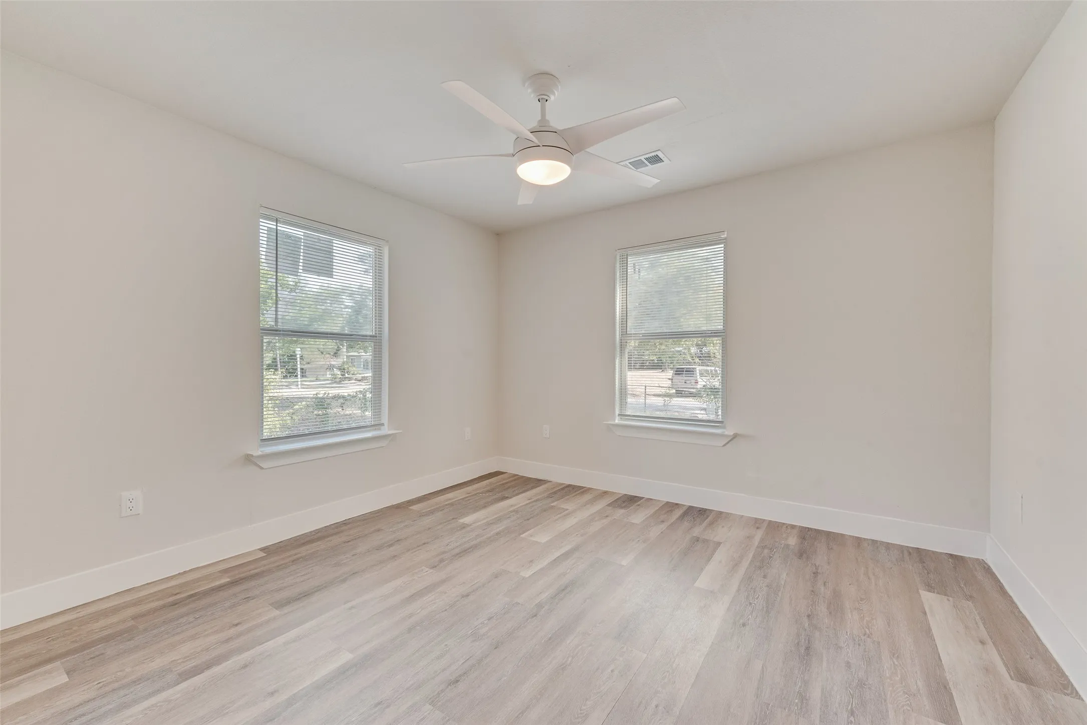 Light wood-finish flooring, white walls, and a ceiling fan with integrated lighting