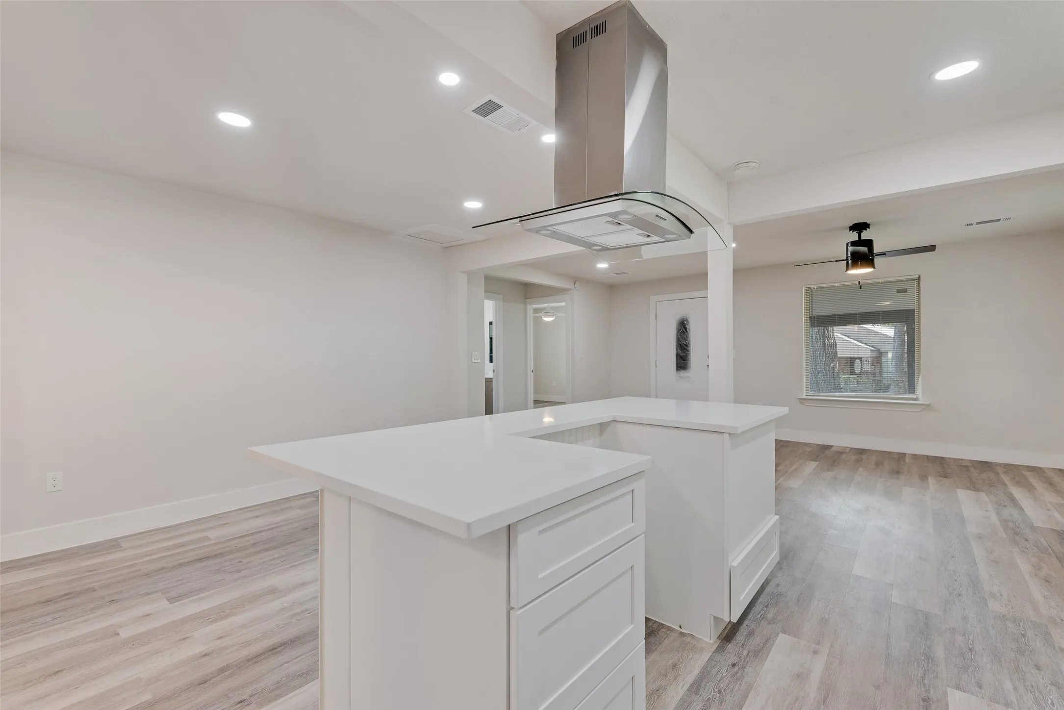 Open-concept living space with wood-finish flooring, recessed lighting, and a kitchen island featuring white cabinetry and light-toned countertops