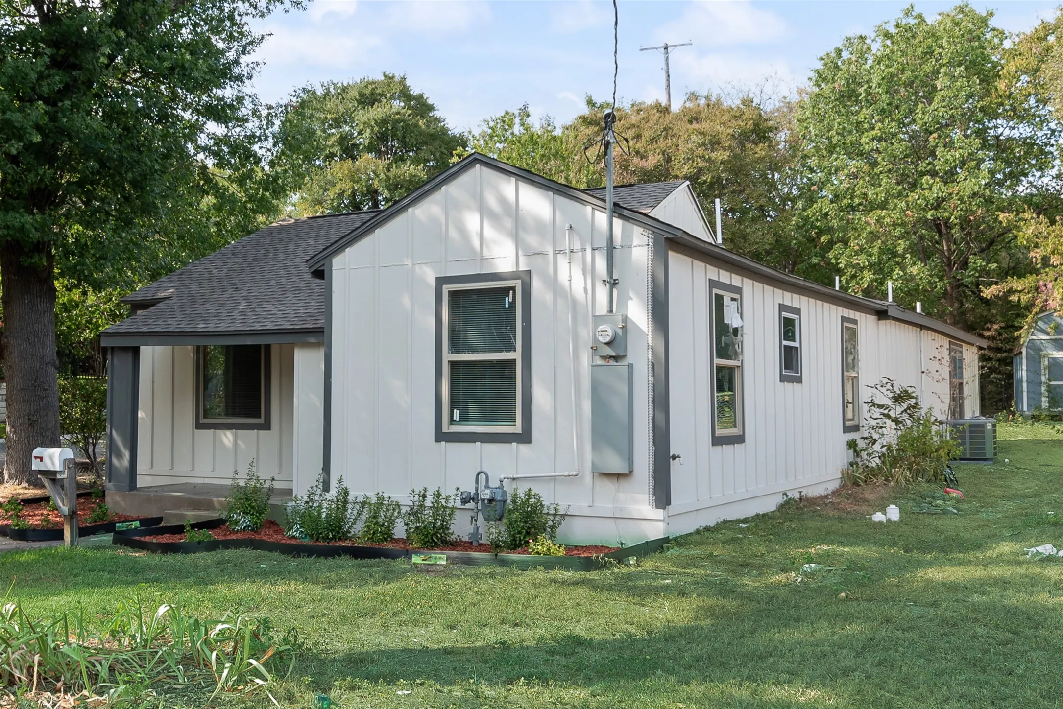 White vertical siding exterior with dark trim, a covered front entry, and a dark shingle roof