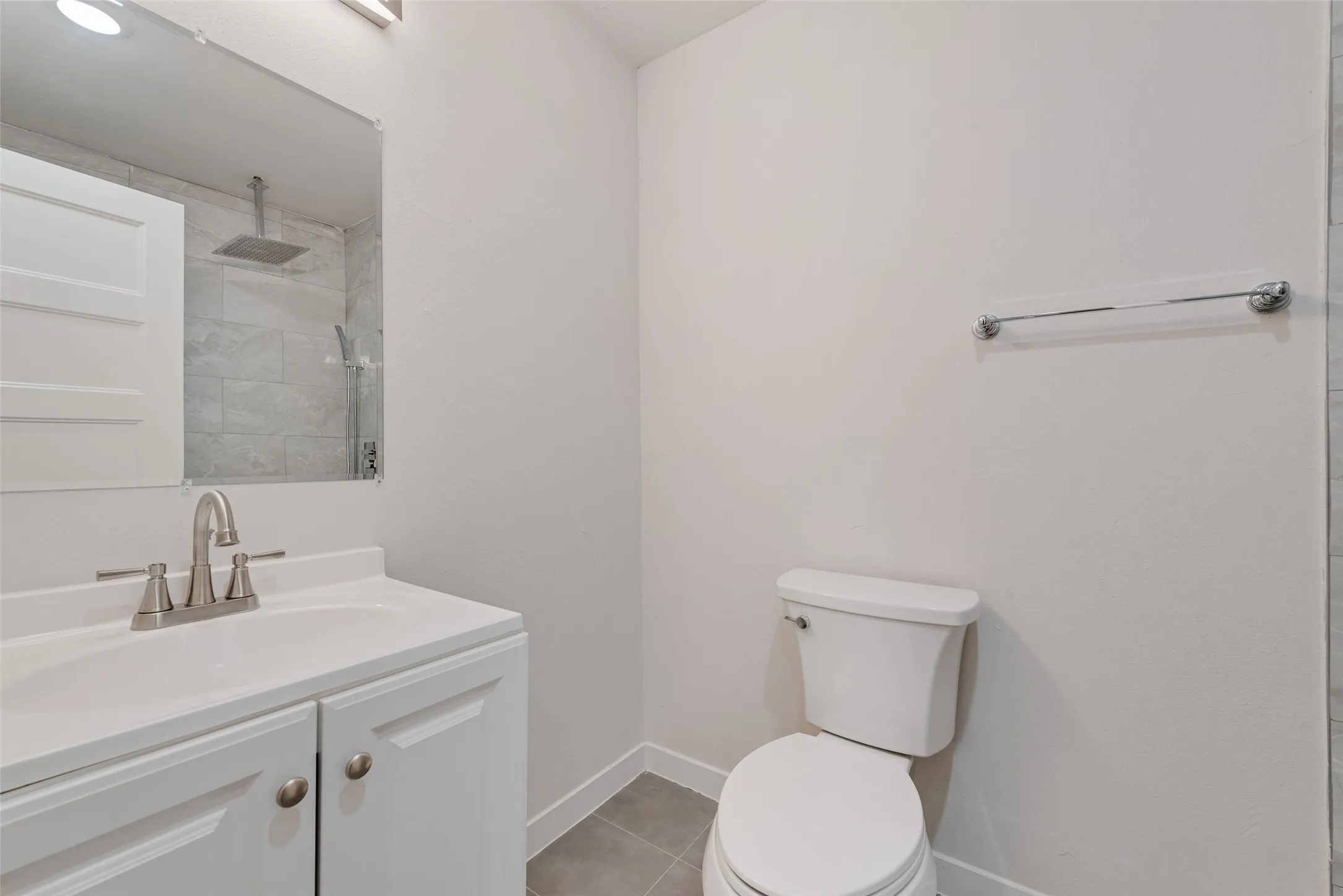 White vanity with integrated sink, brushed nickel faucet, frameless mirror, and neutral floor tiling
