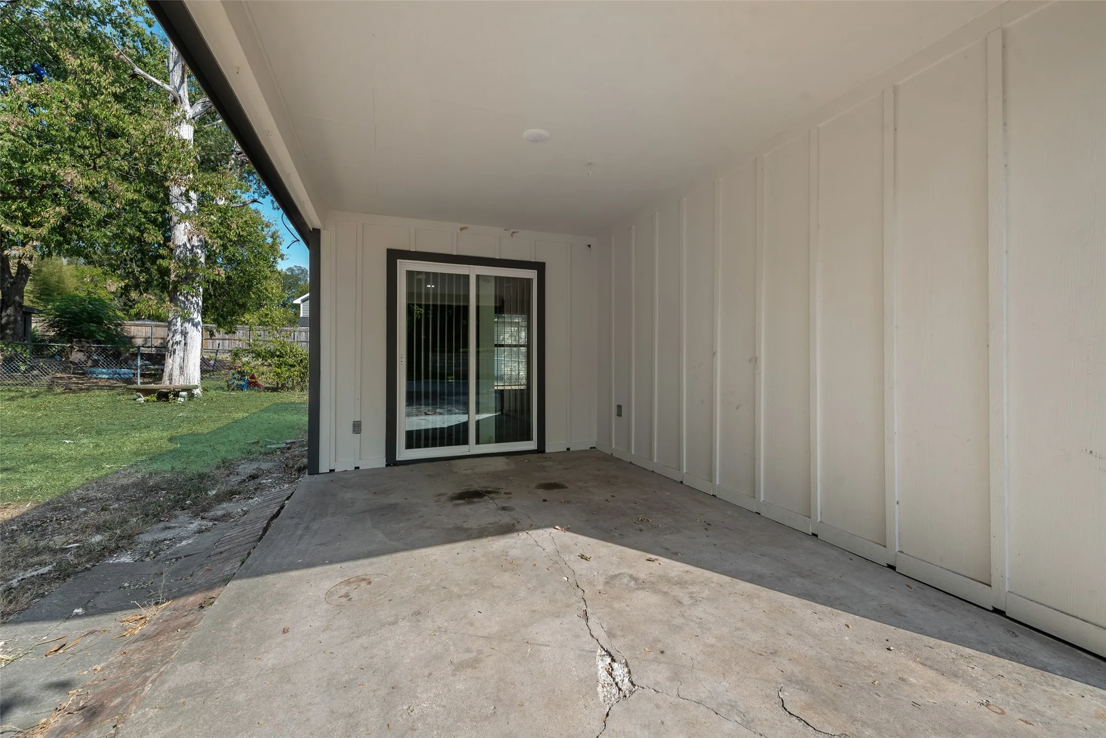 Covered patio area with concrete surfacing, white board and batten siding, and a sliding glass door