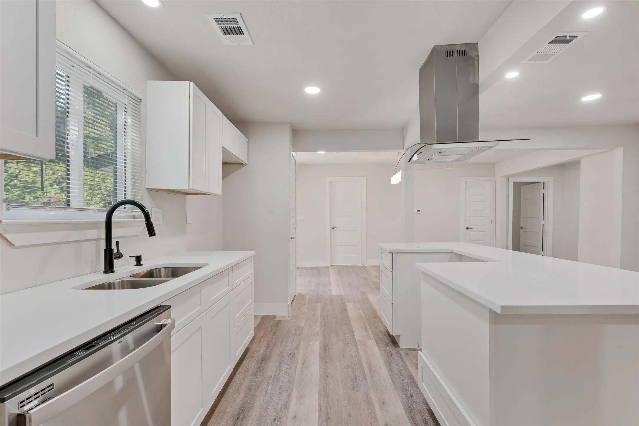 Contemporary kitchen featuring white cabinetry, light-toned countertops, stainless steel appliances, a black matte faucet, and wood-finish flooring