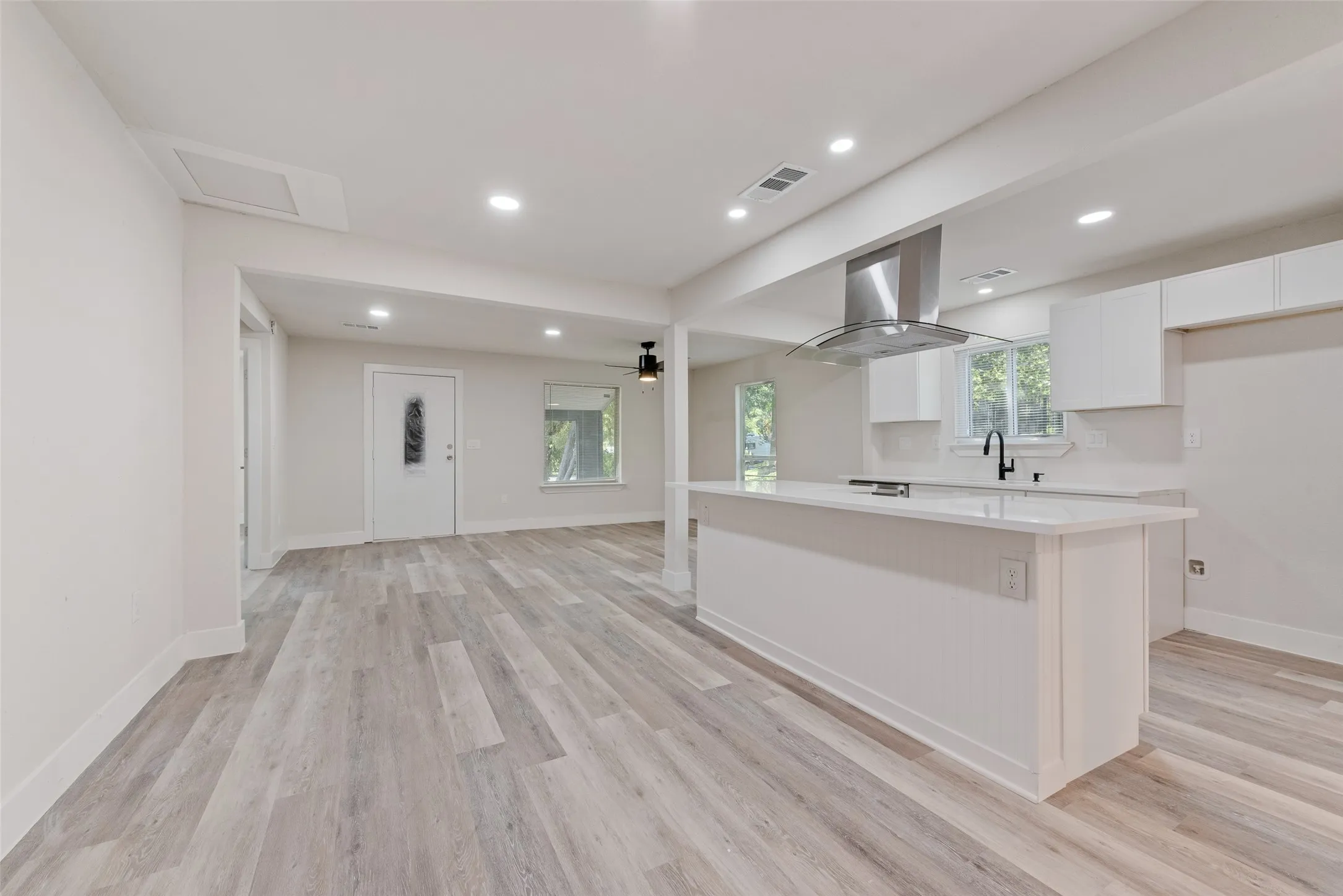 Open-concept living area featuring wood-finish flooring, recessed lighting, a kitchen island with a smooth countertop, white cabinetry, and a stainless steel range hood