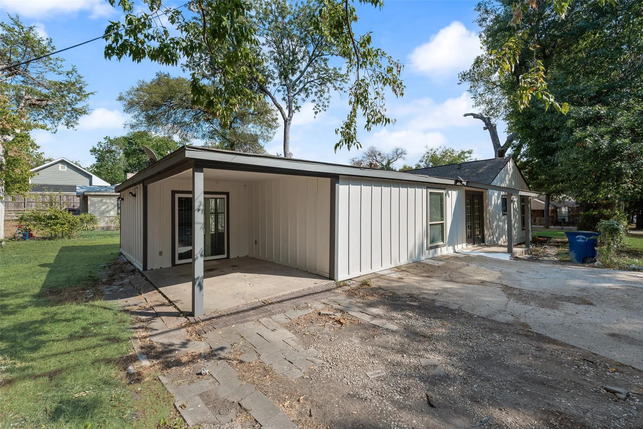 Exterior siding with dark trim accents, covered patio area, sliding glass door entry, gravel driveway, and a gabled roofline