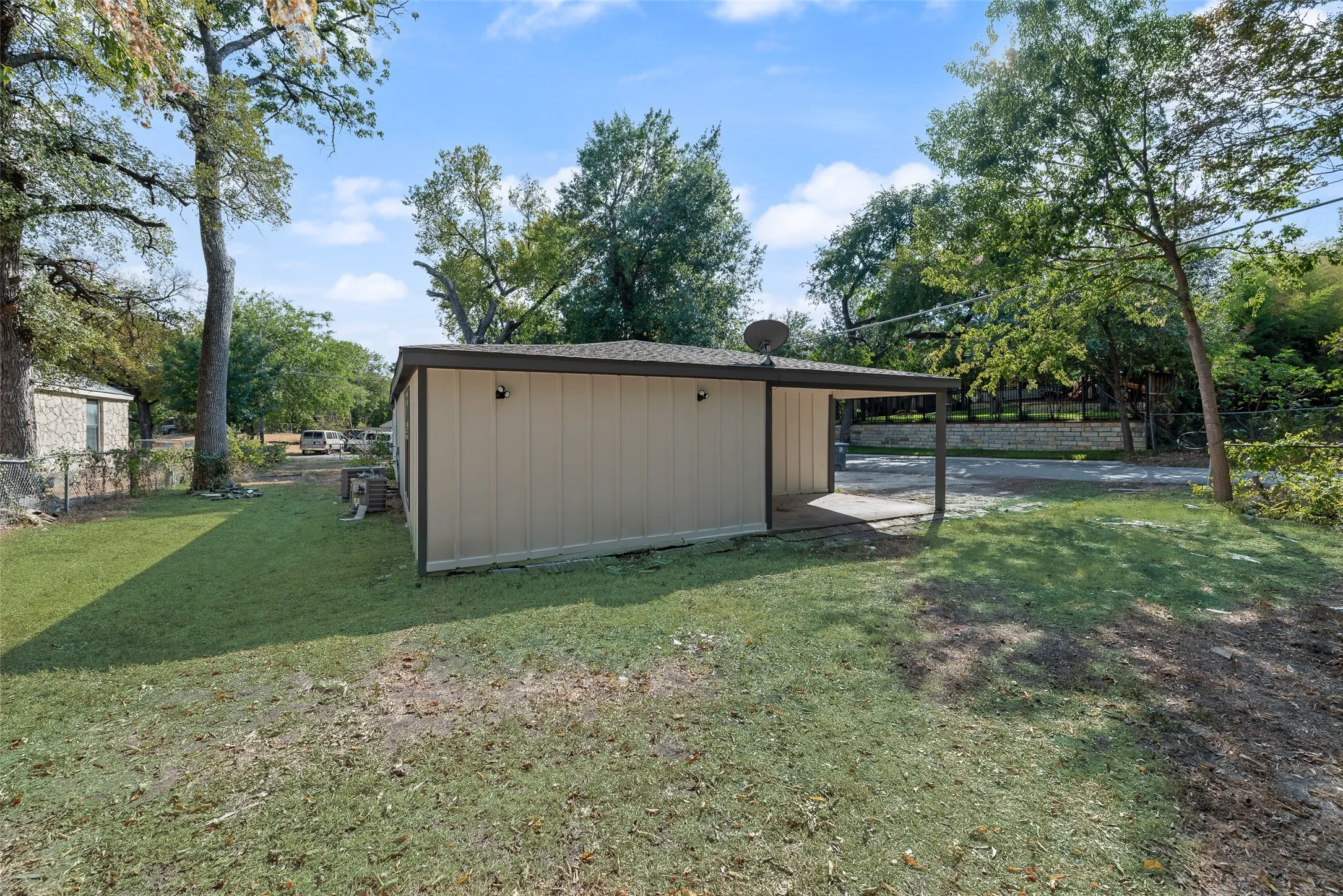 Spacious lawn area, covered patio, mature trees, and a stone retaining wall