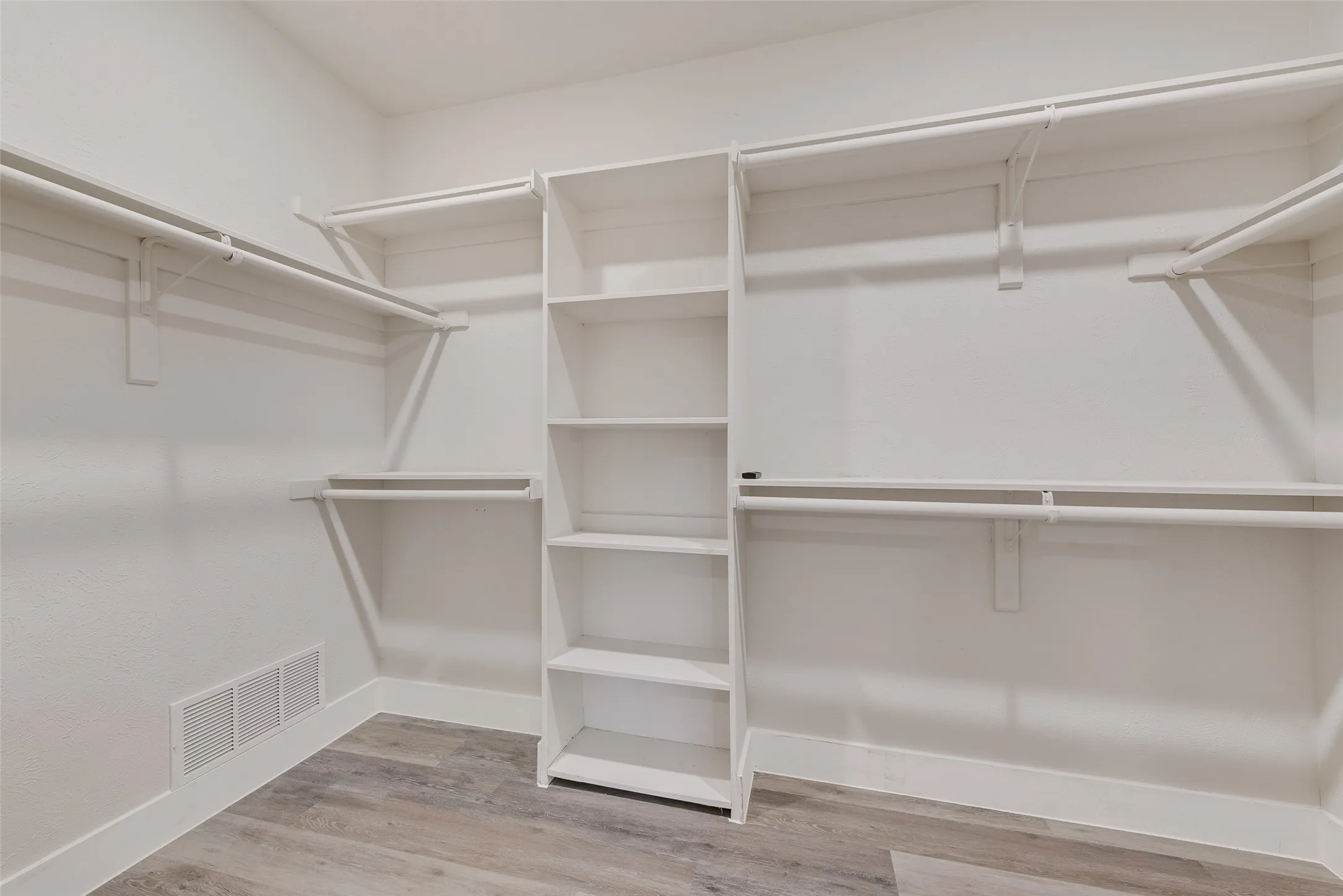Integrated shelving system, multiple hanging rods, corner shelving unit, wood-finish flooring, and white walls